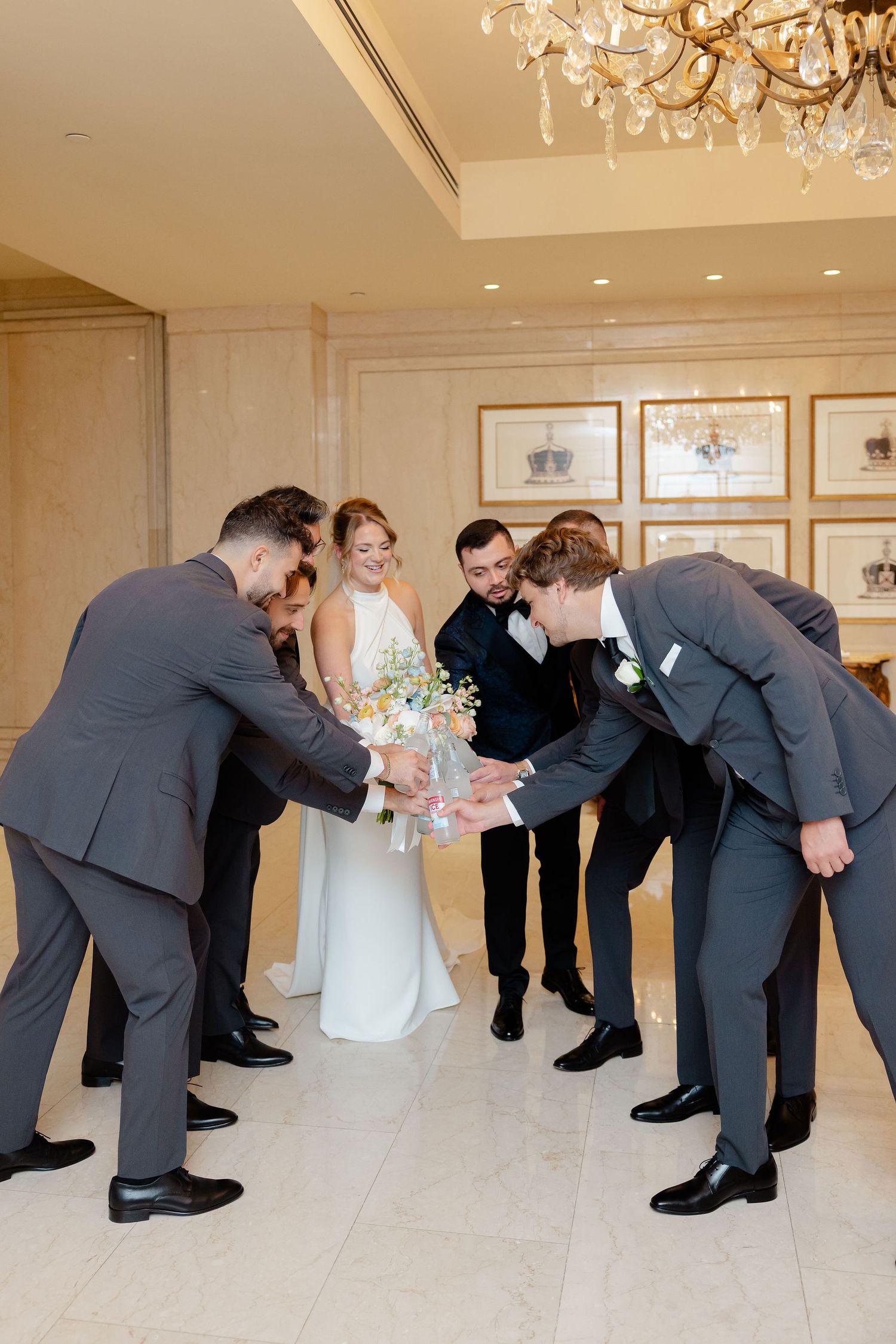Wedding party members bow dramatically in sequence across an elegant ballroom with chandeliers.