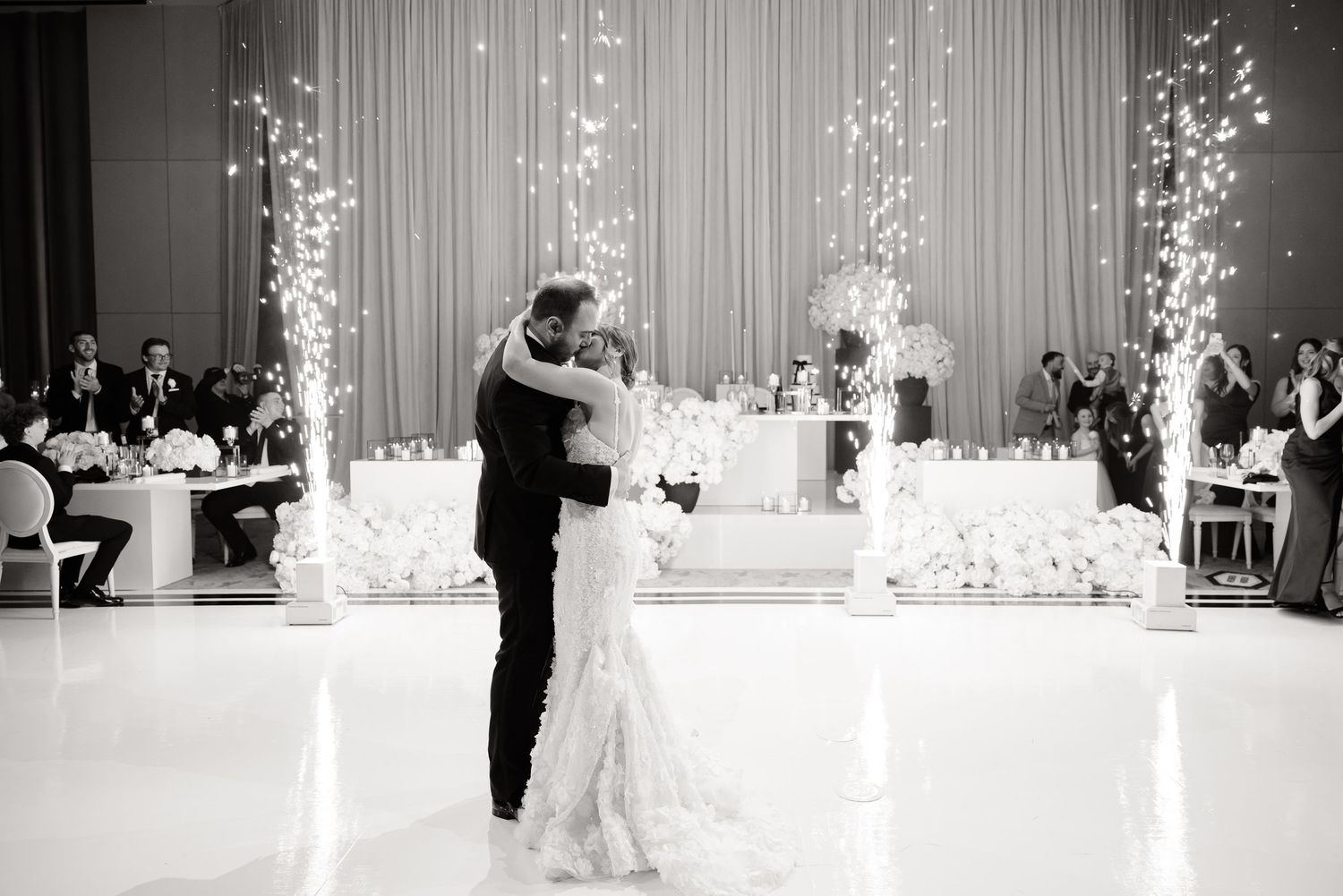 A romantic first dance between newlyweds at an elegant wedding reception with glowing white decor and florals.