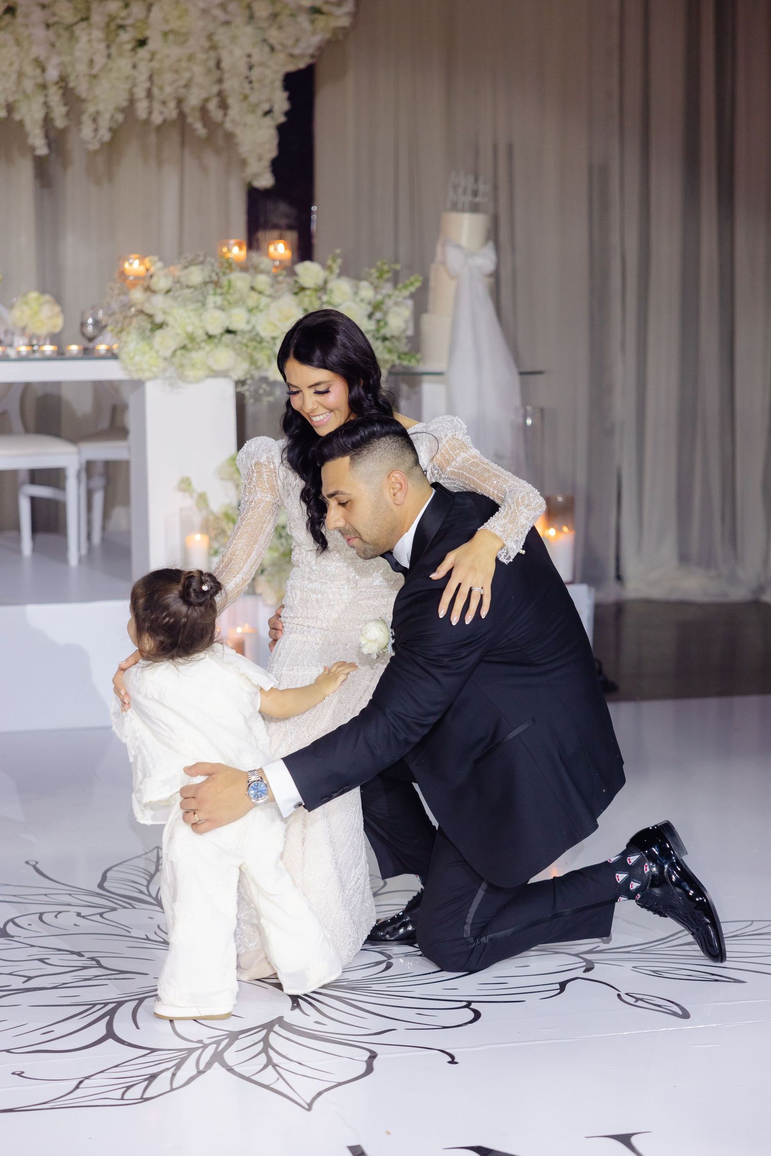 Family shares tender moment on decorated wedding dance floor with floral arrangements.