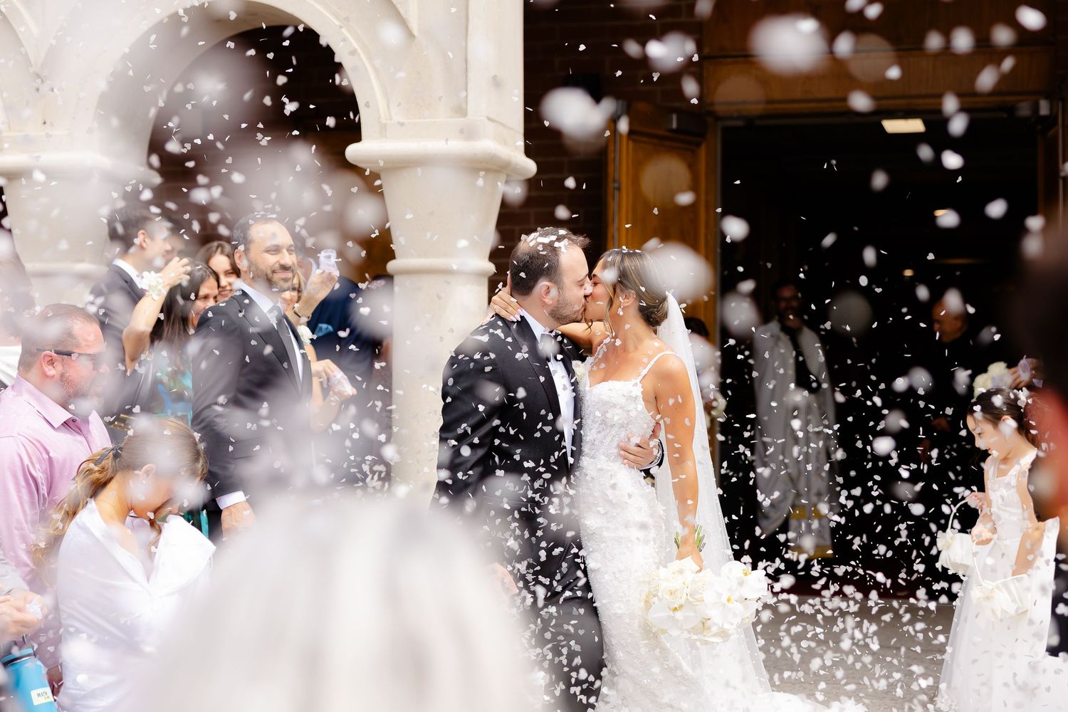 Newlyweds share a romantic kiss as guests shower them with white rice outside a church on their wedding day.