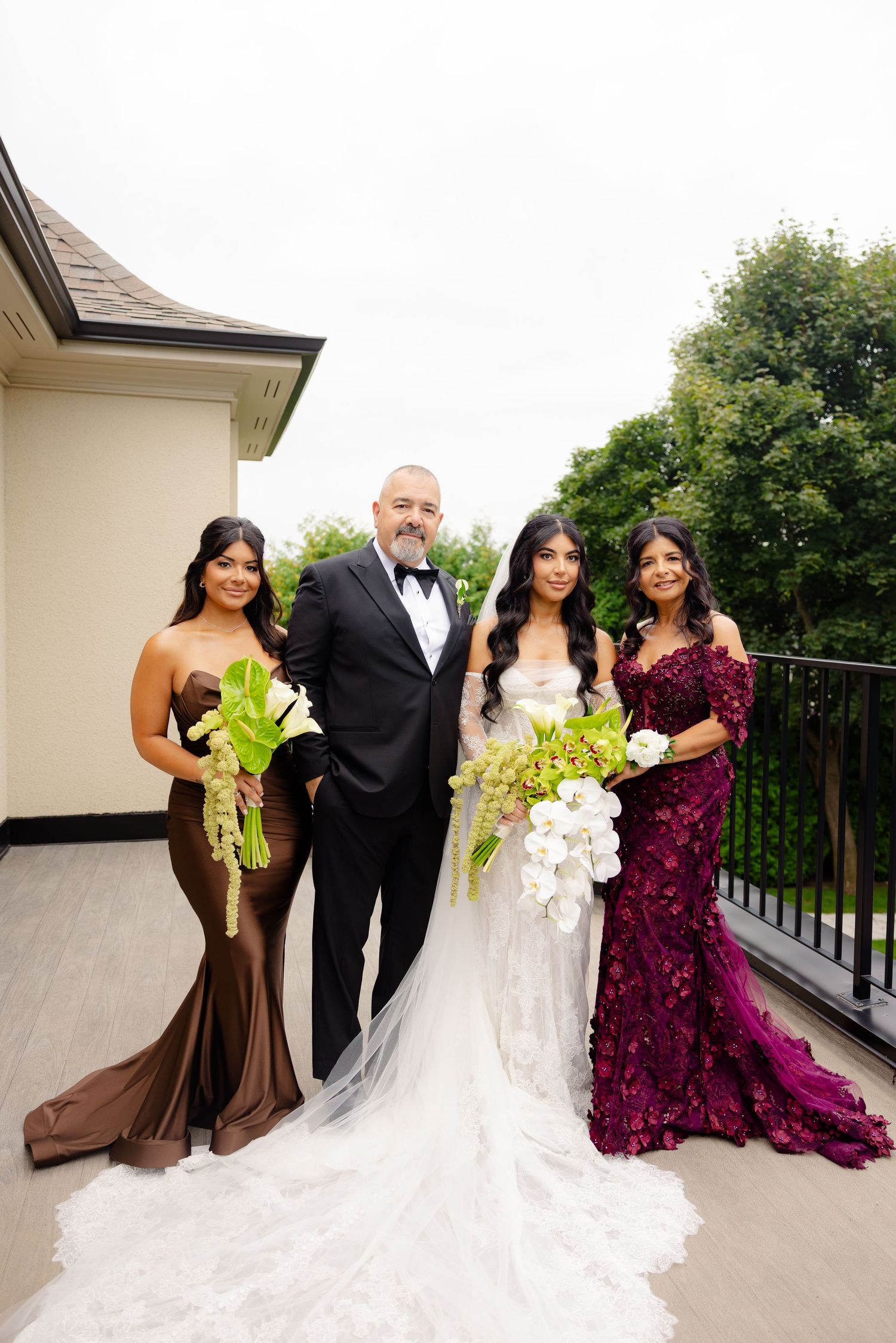 Wedding party poses on balcony in burgundy and brown bridesmaids dresses with elegant white bridal gown.