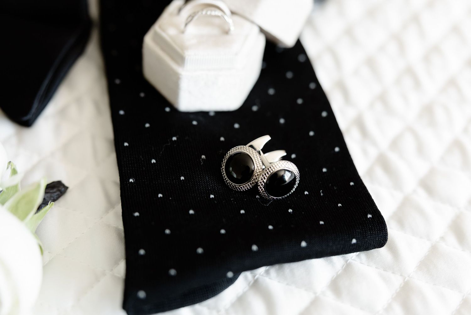 Silver cufflinks with black gemstones displayed on a black polka dot fabric next to a small white box.