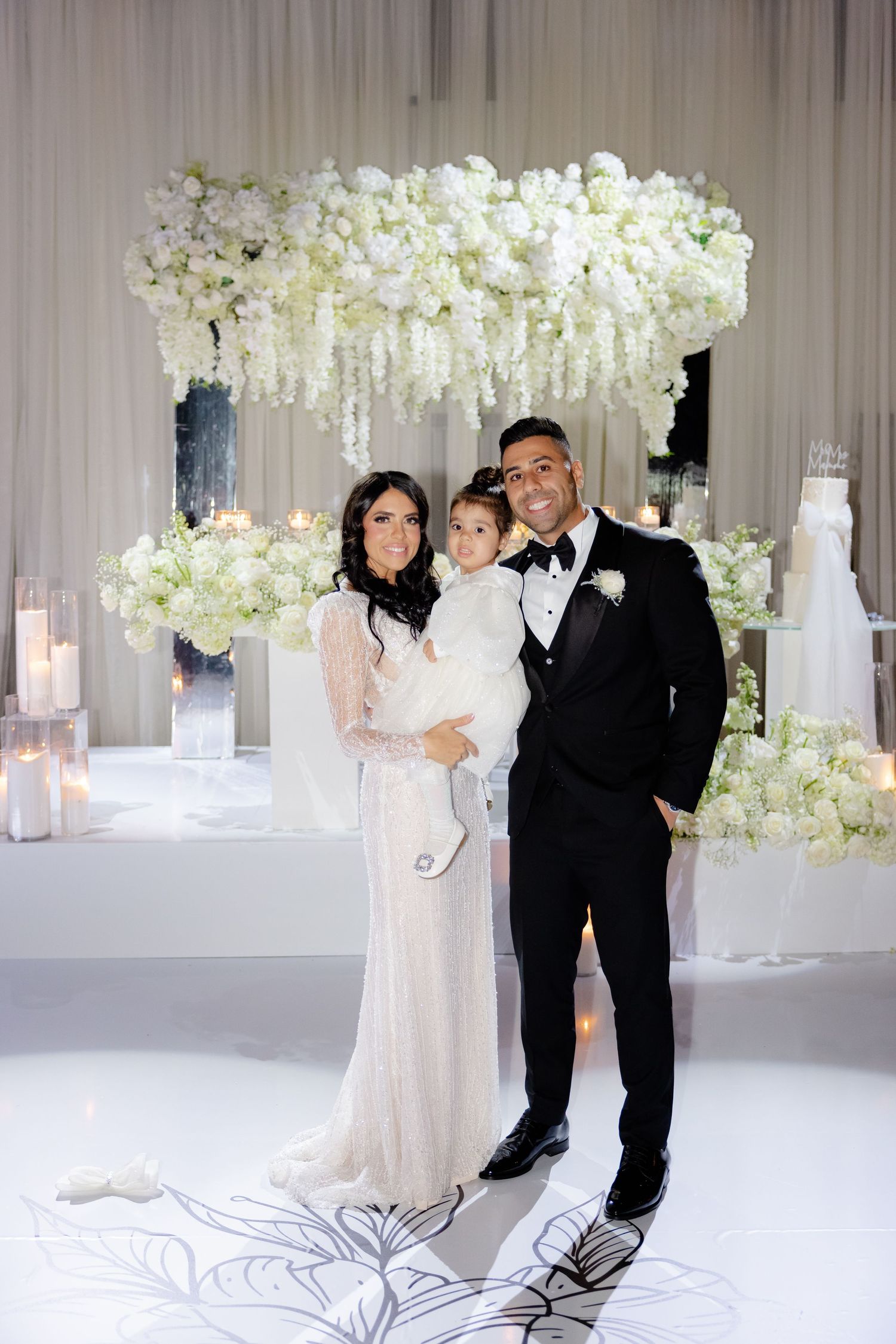 Wedding celebration features elegant white floral arrangements and a decorated stage.