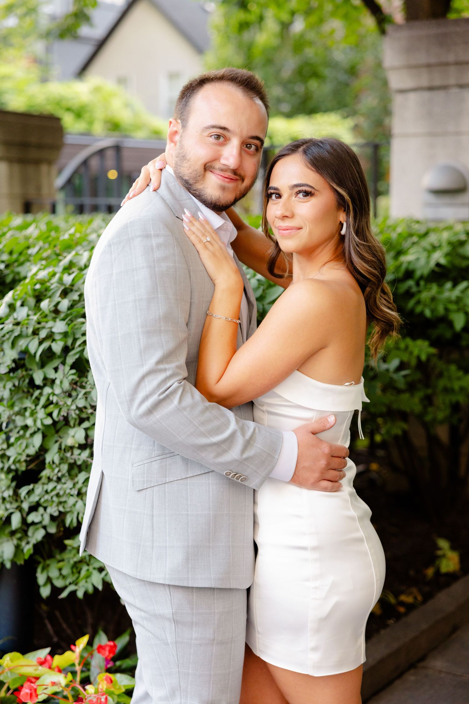 Couple in matching summer formal wear pose together by garden entrance.