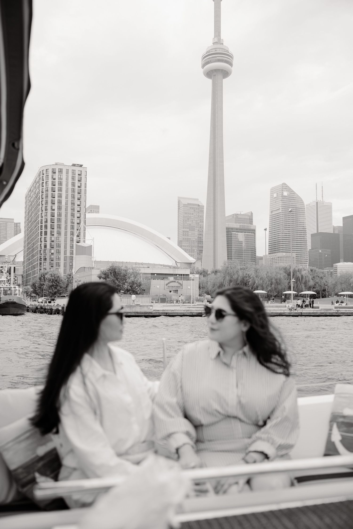 Two people enjoy a boat ride with Toronto's iconic CN Tower and Rogers Centre stadium visible in the city skyline.