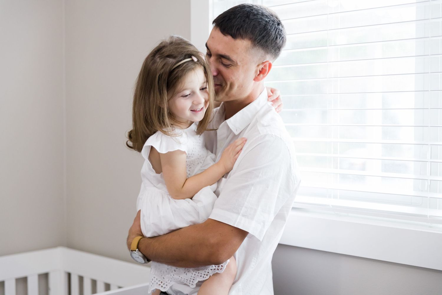 Parent and child in white clothes share a special moment by a window.