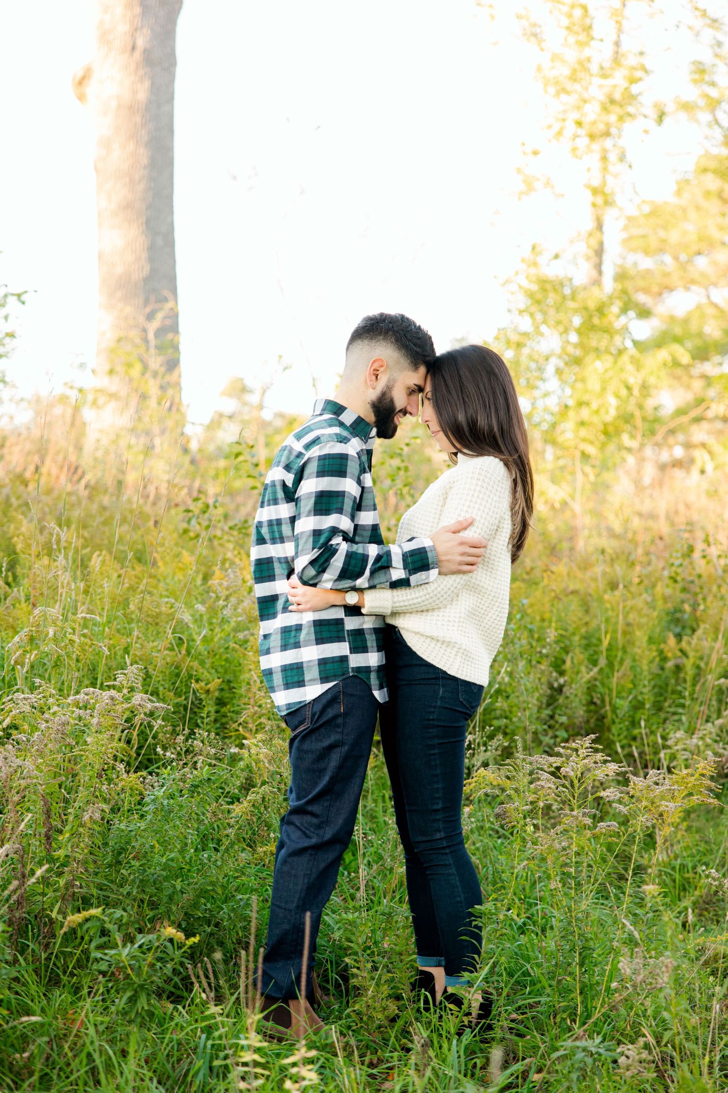 Couple in casual wear embracing in tall grass during golden hour.