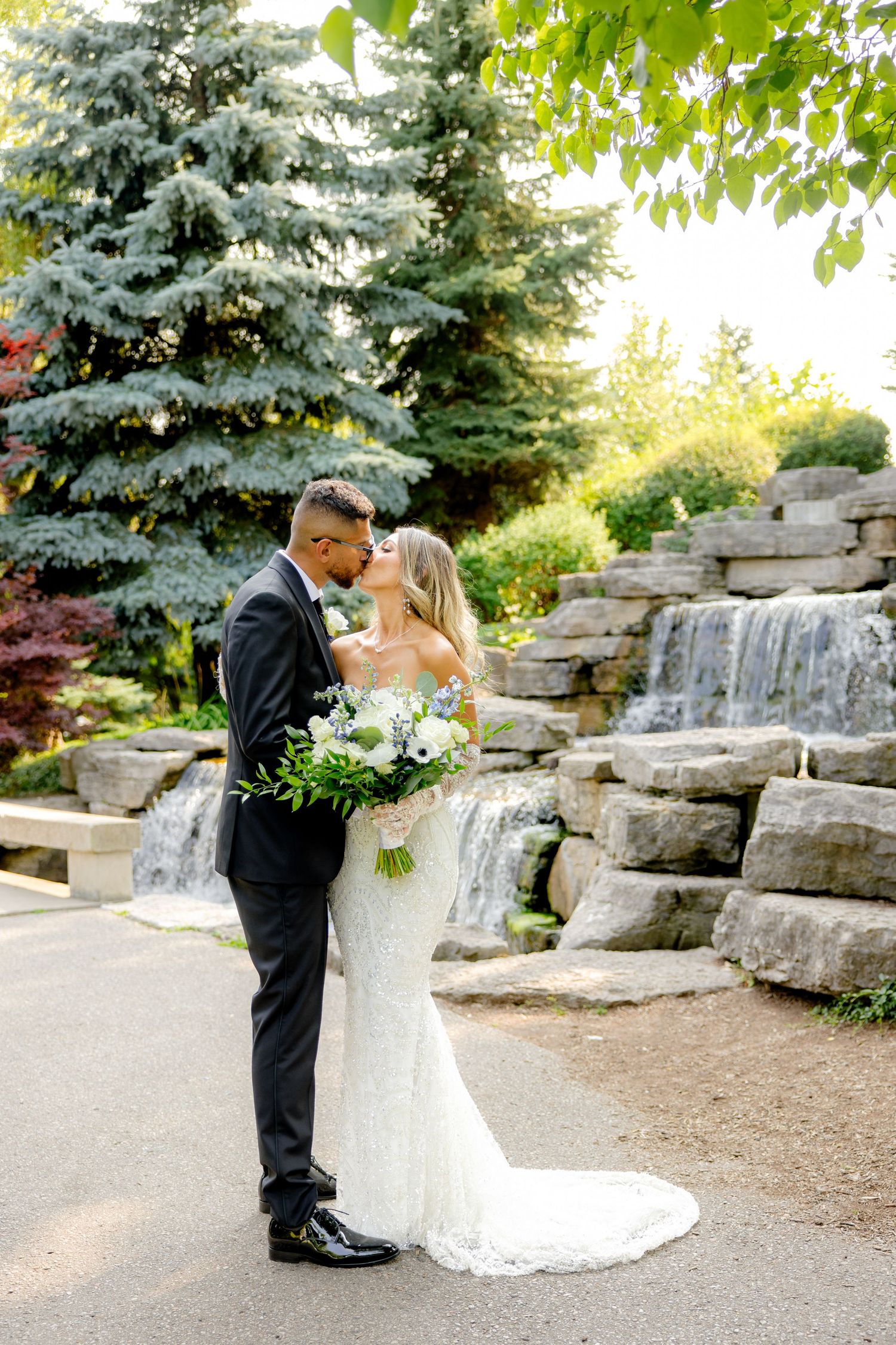 A romantic wedding portrait captured in front of a stone waterfall feature and blue spruce trees.