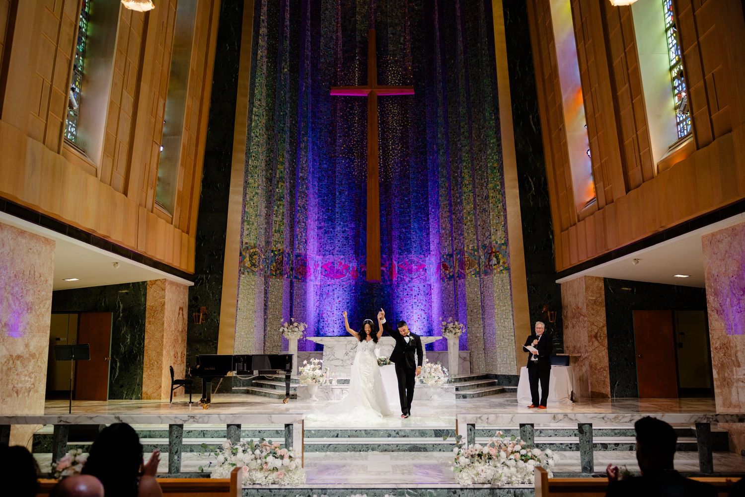 Wedding ceremony in progress at elevated church altar with purple lighting and cross backdrop.