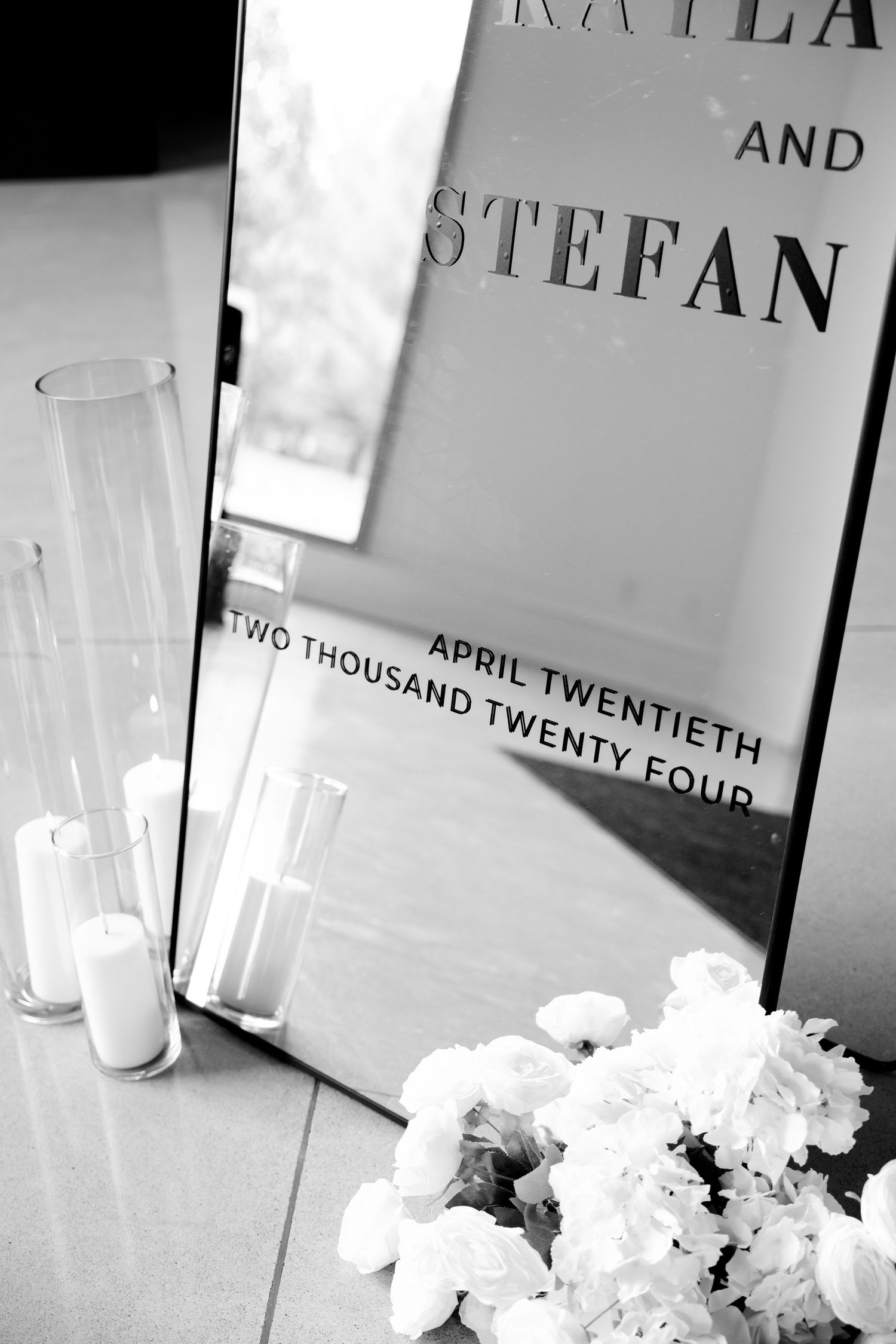 Artistic black and white detail of wedding welcome sign with candles and flowers.