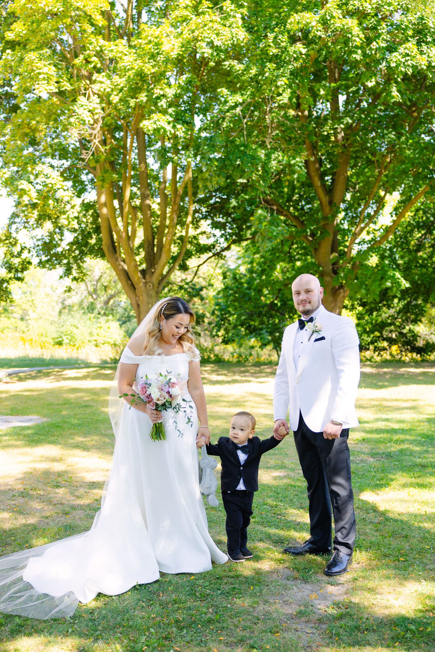 Joyful wedding portrait outdoors featuring couple and small child in formal attire.