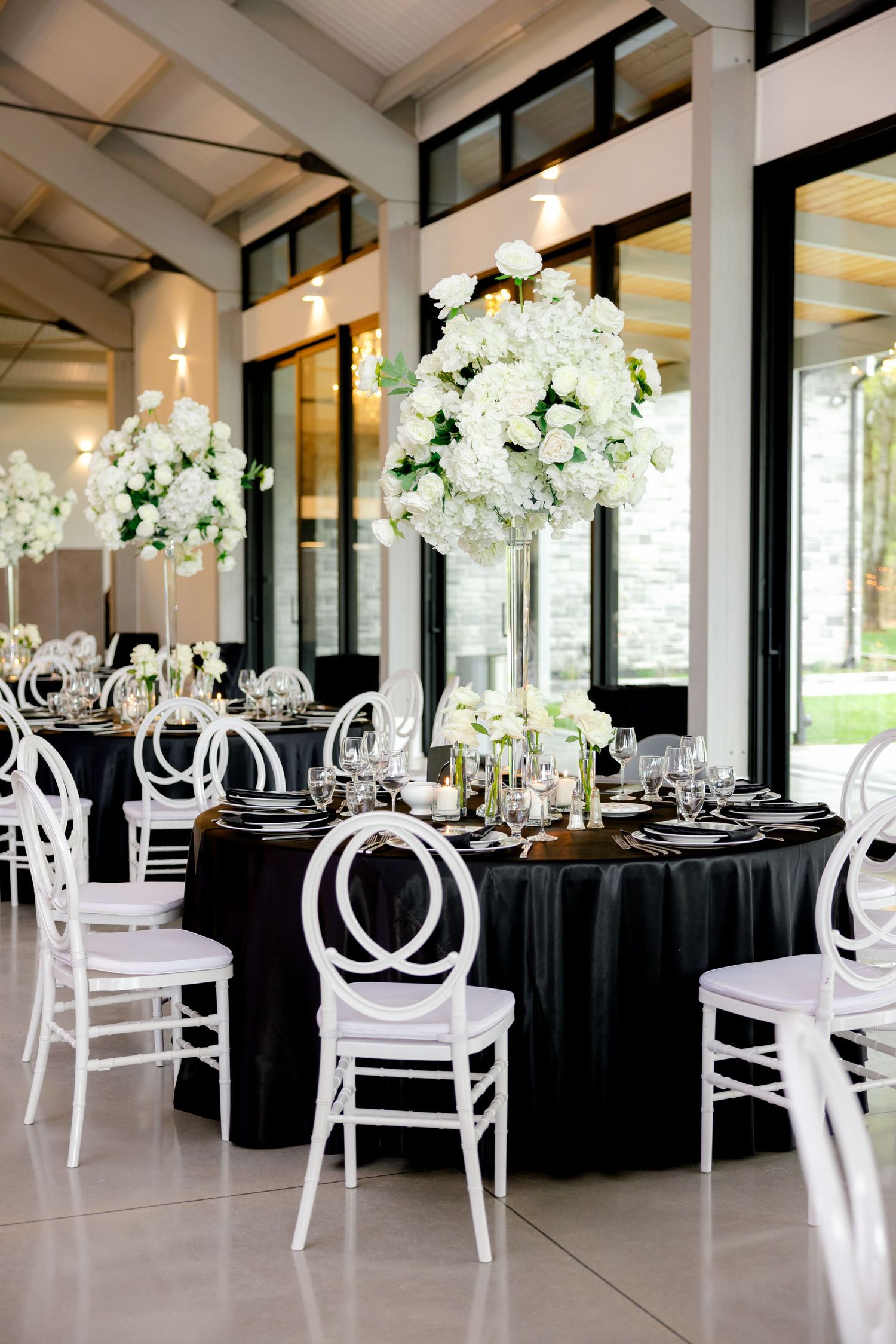Modern wedding reception venue with black tablecloths, white chairs, and towering white floral centerpieces.