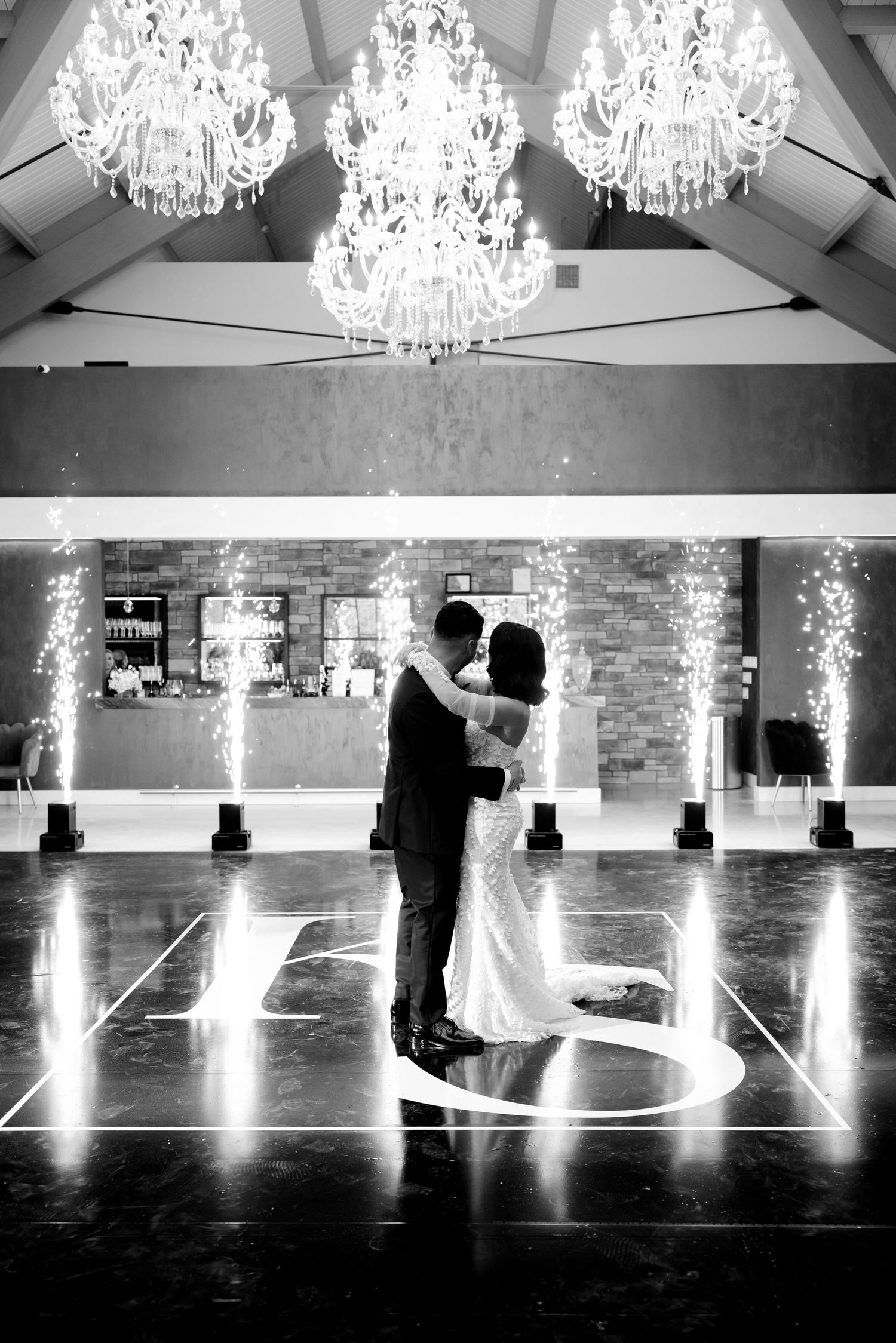 Romantic couple dances under chandeliers with illuminated floor design and sparkler effects.