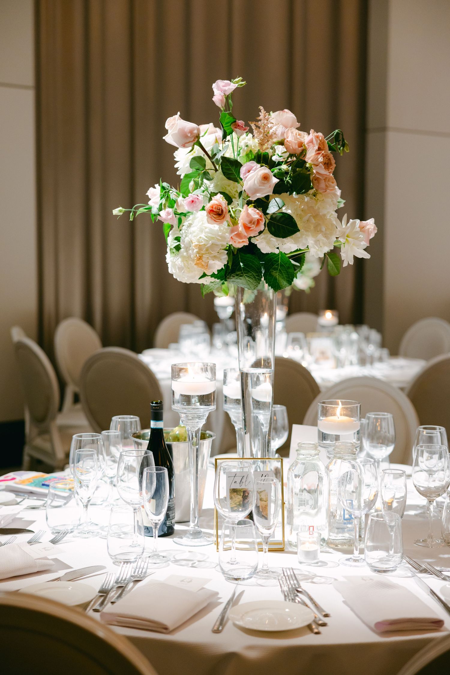 Elegant wedding table setting with tall peach and white floral centerpiece and crystal glassware.