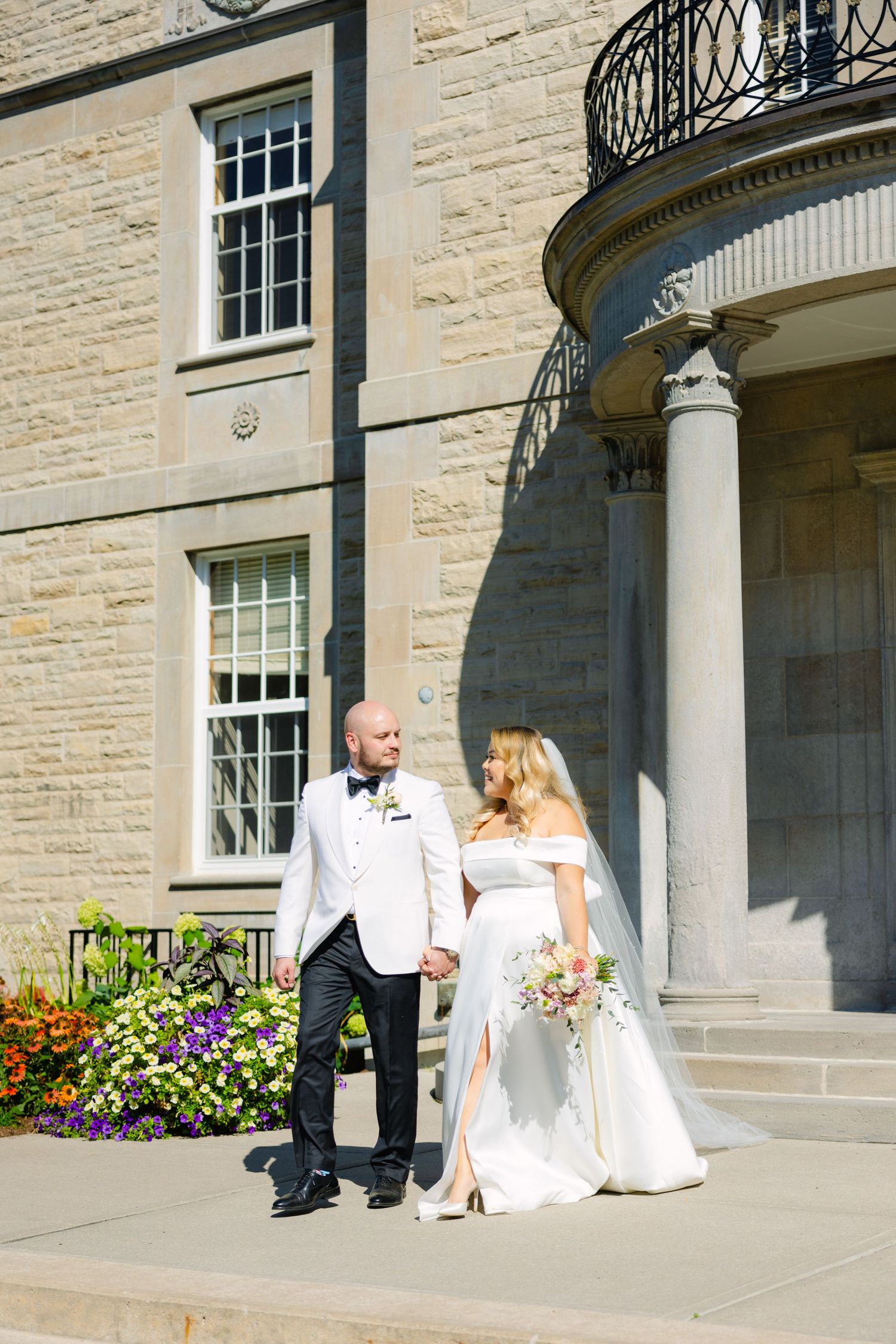 Sunlit wedding photography against classic limestone architecture with blooming garden flowers.