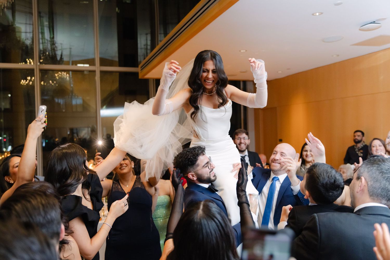 Newlywed bride being lifted up by wedding guests during a celebratory hora dance at an elegant reception.