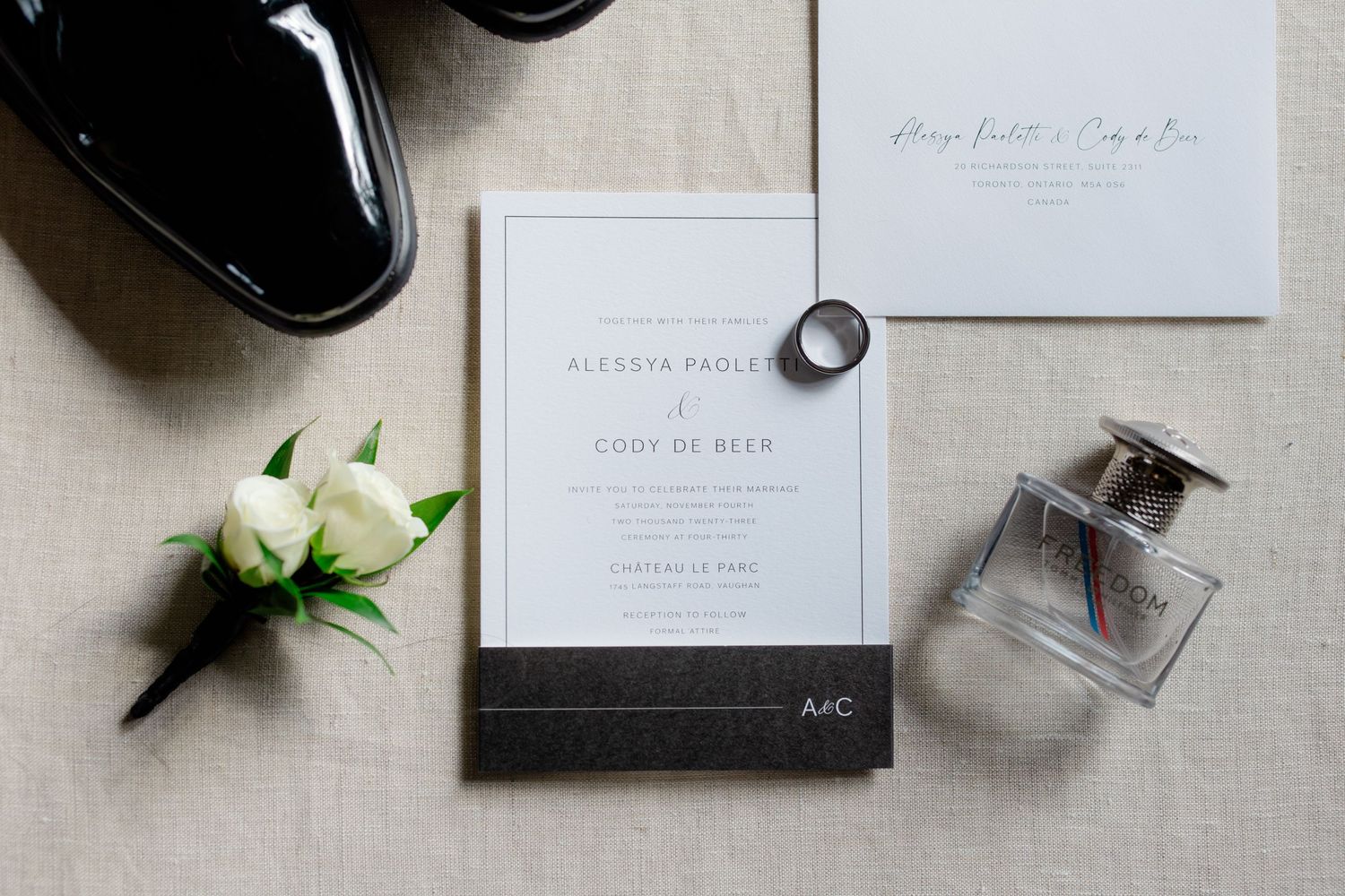 Wedding invitation and details flatlay with perfume bottle, white rose, and black shoes.