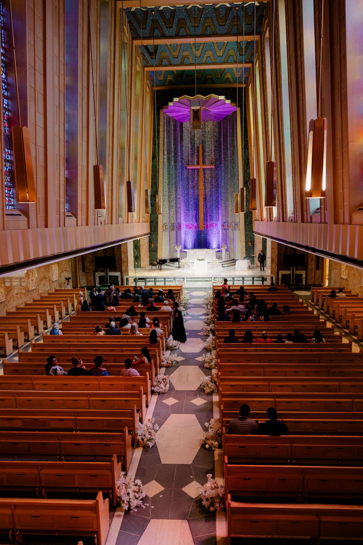 Gothic church interior with wooden pews and purple-lit altar during wedding ceremony.