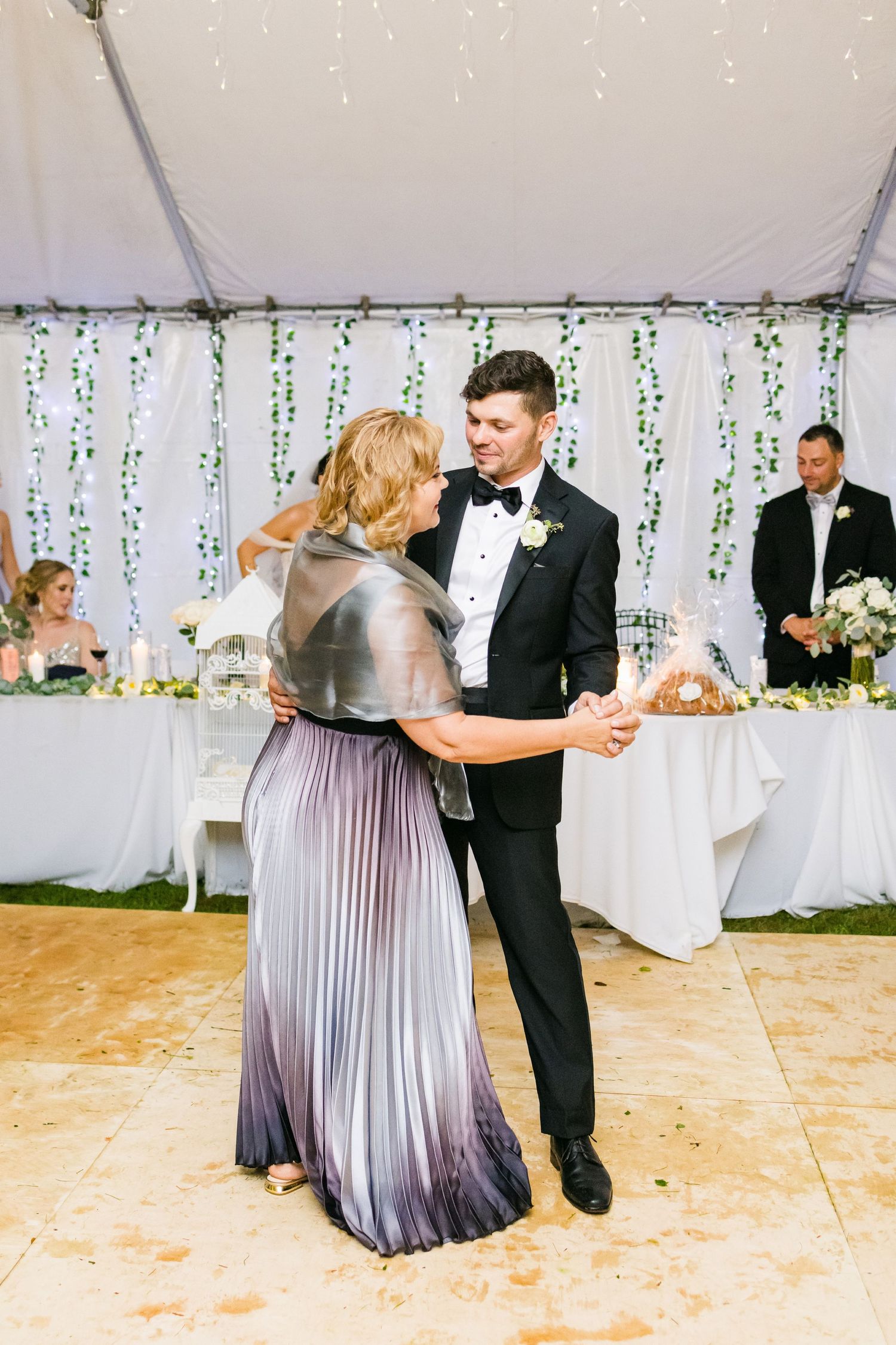 Dance moment at wedding reception with formal attire under white tent with string lights.