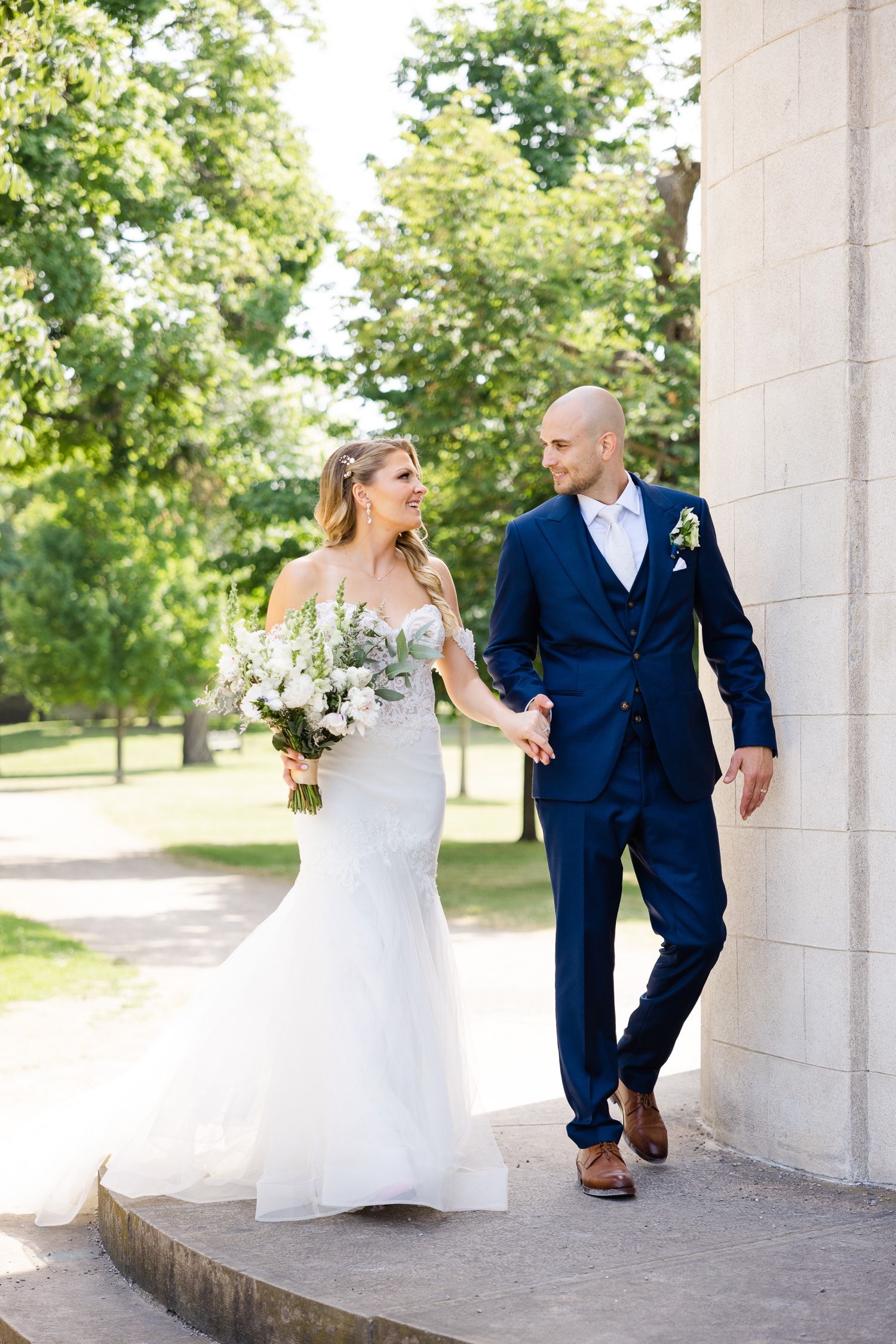 Couple standing together on stone porch with white floral bouquet.