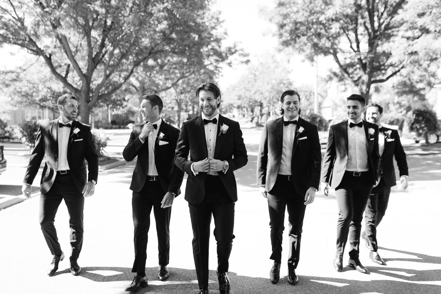 Wedding party walking together in black and white photo on tree-lined path.