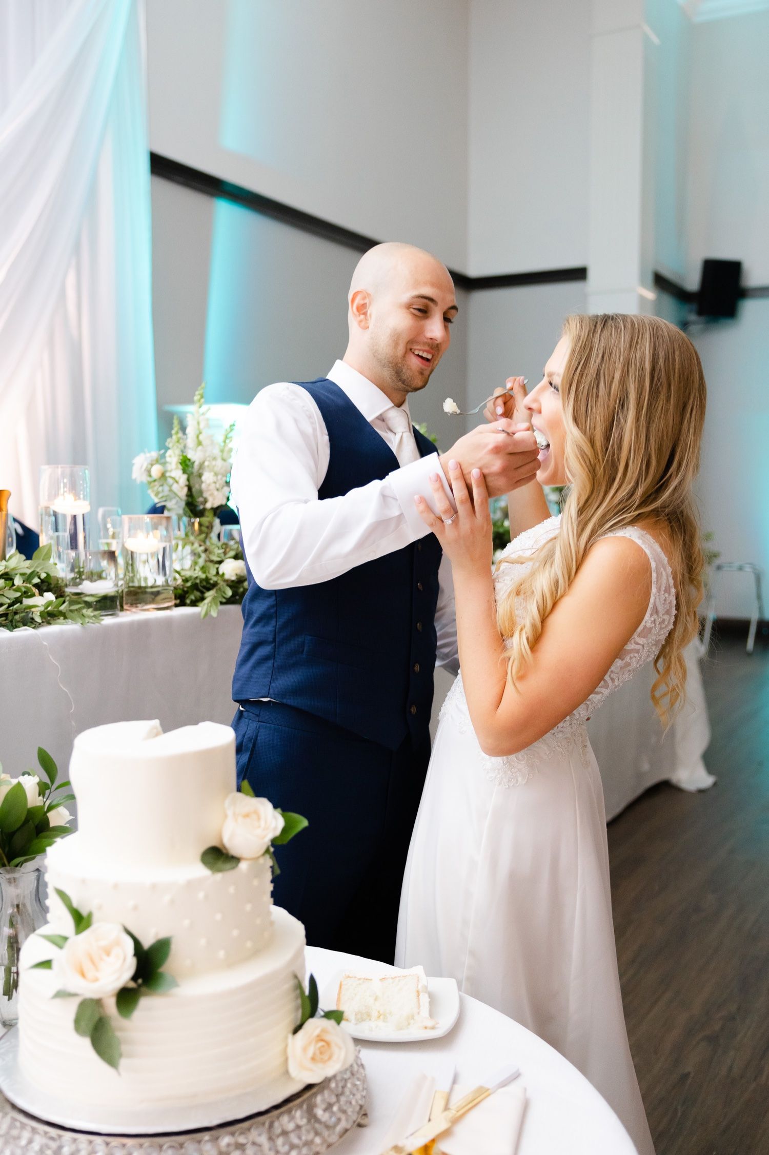 A couple playfully feeds each other wedding cake at their reception.