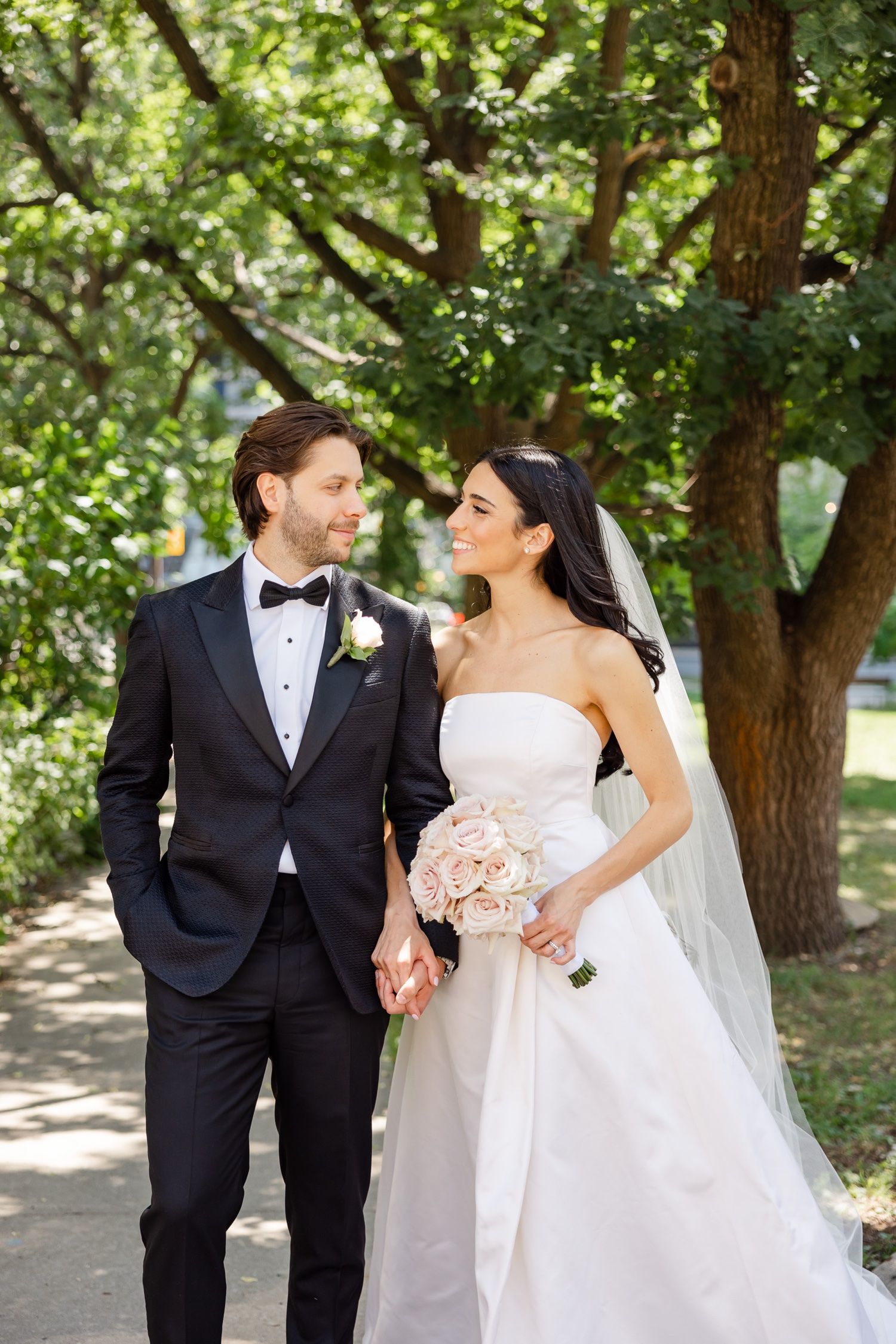 Romantic wedding portrait of couple on tree-lined path with soft natural lighting.