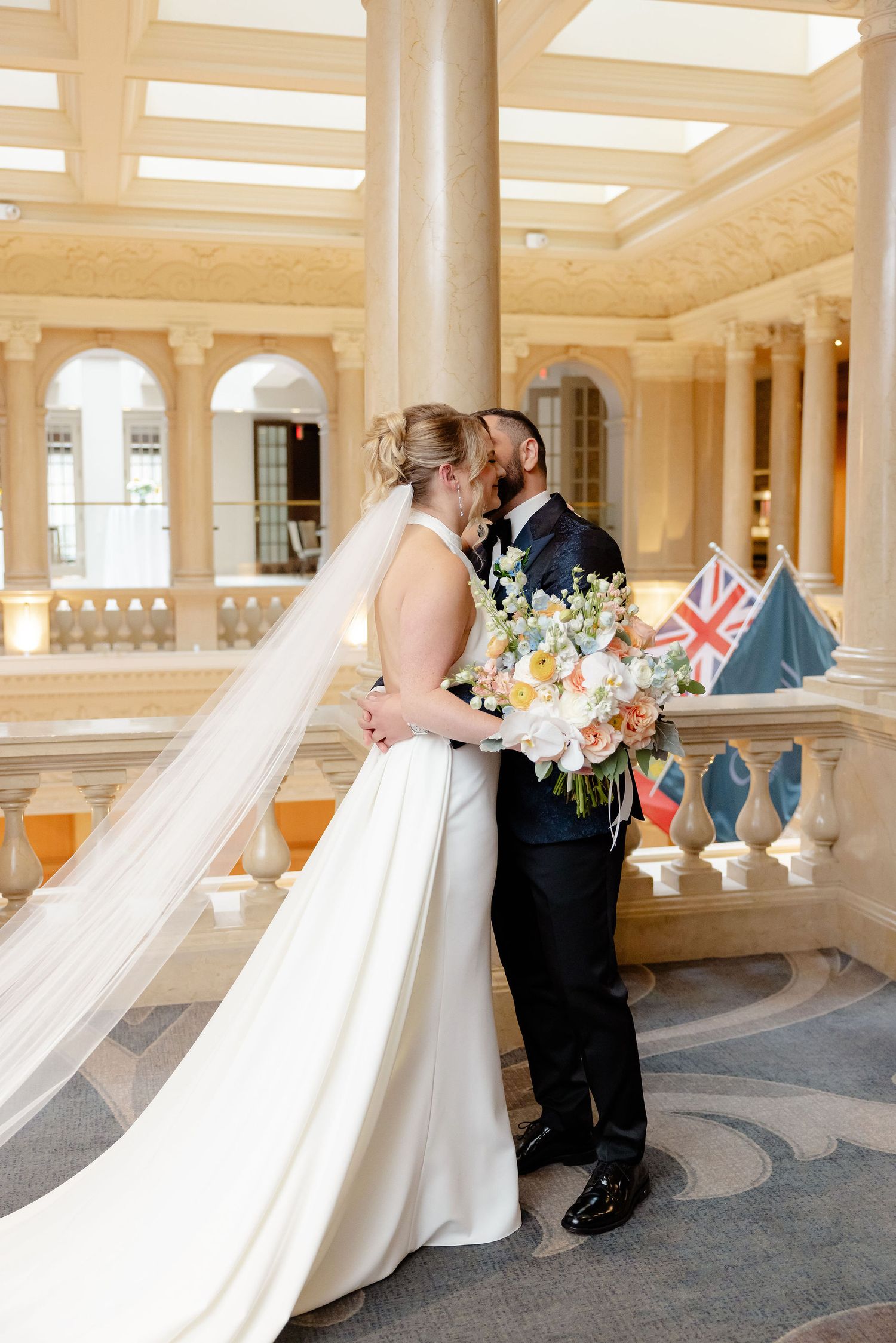 Wedding couple sharing intimate moments in a grand hallway with classical architecture.