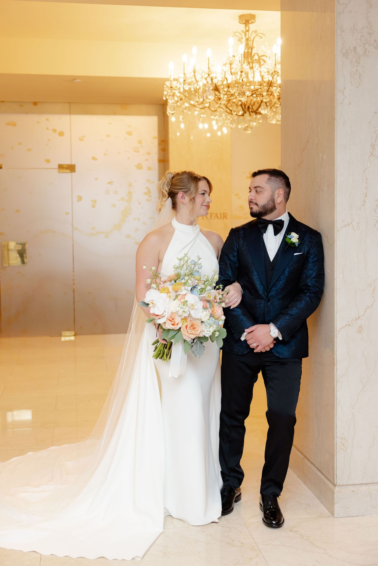A couple shares a romantic first look moment in an elegant venue with crystal chandeliers.