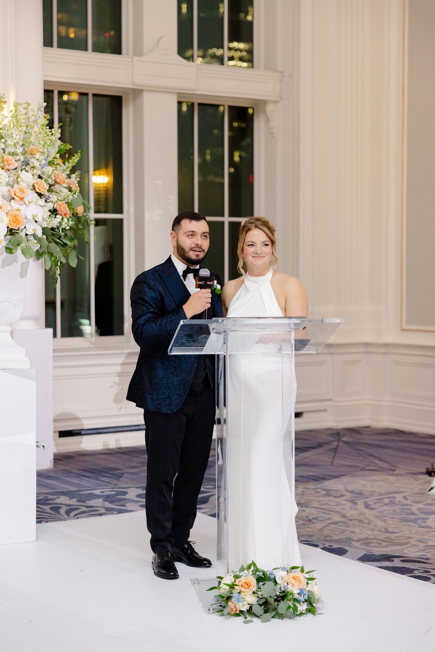 Wedding reception venue decorated with white pedestals and floral arrangements in an elegant ballroom.
