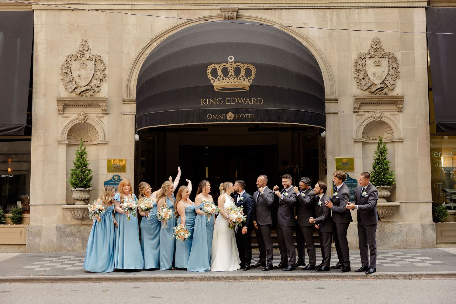 Wedding party poses under grand stone archways with decorative crown emblems on the exterior.