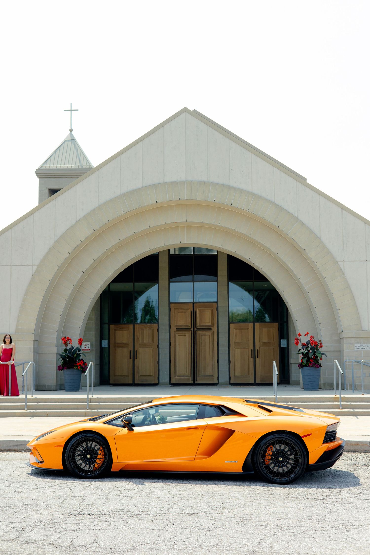 Orange Lamborghini Aventador parked in front of modern white church entrance.