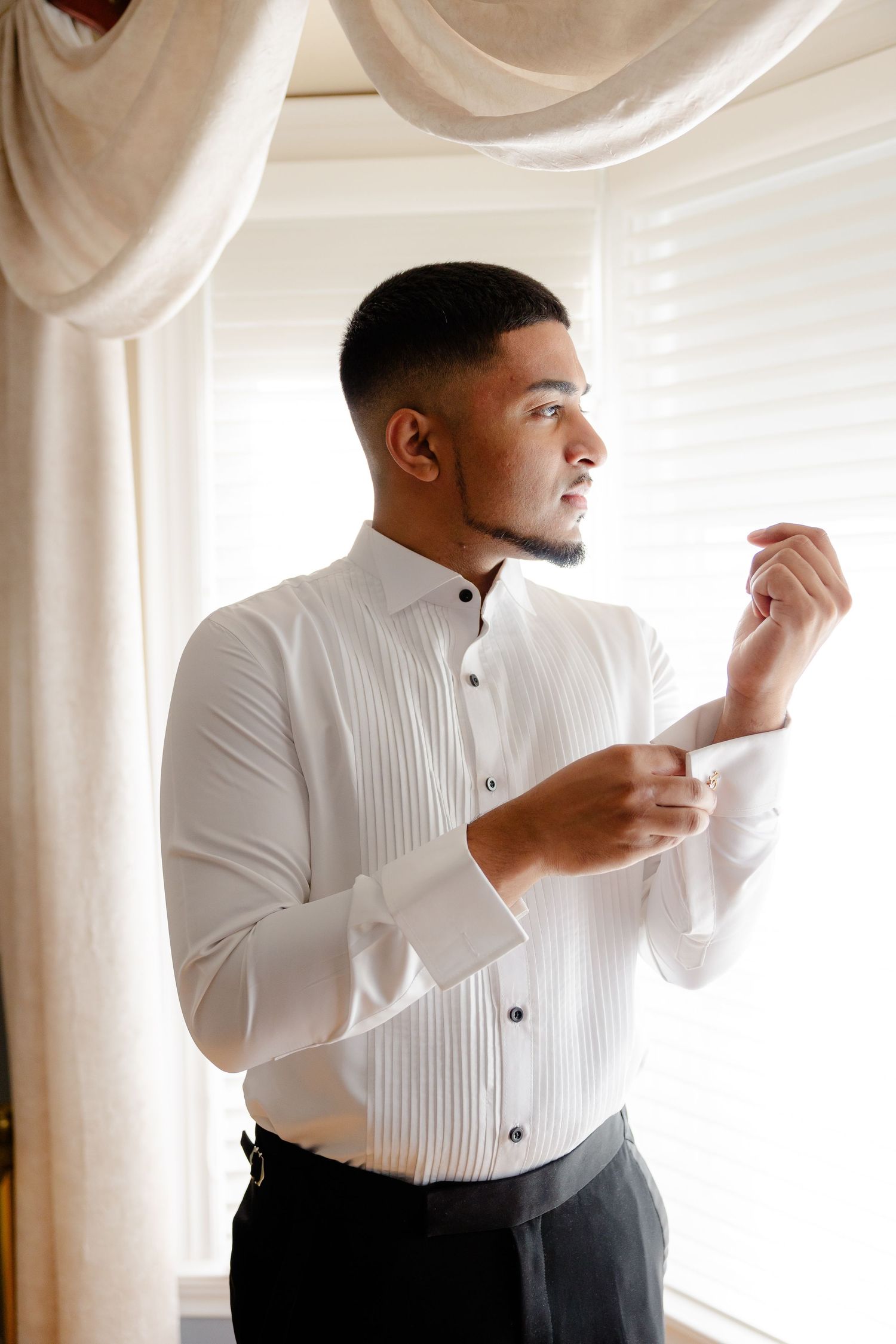 Person in white dress shirt adjusting sleeve cuff by window.