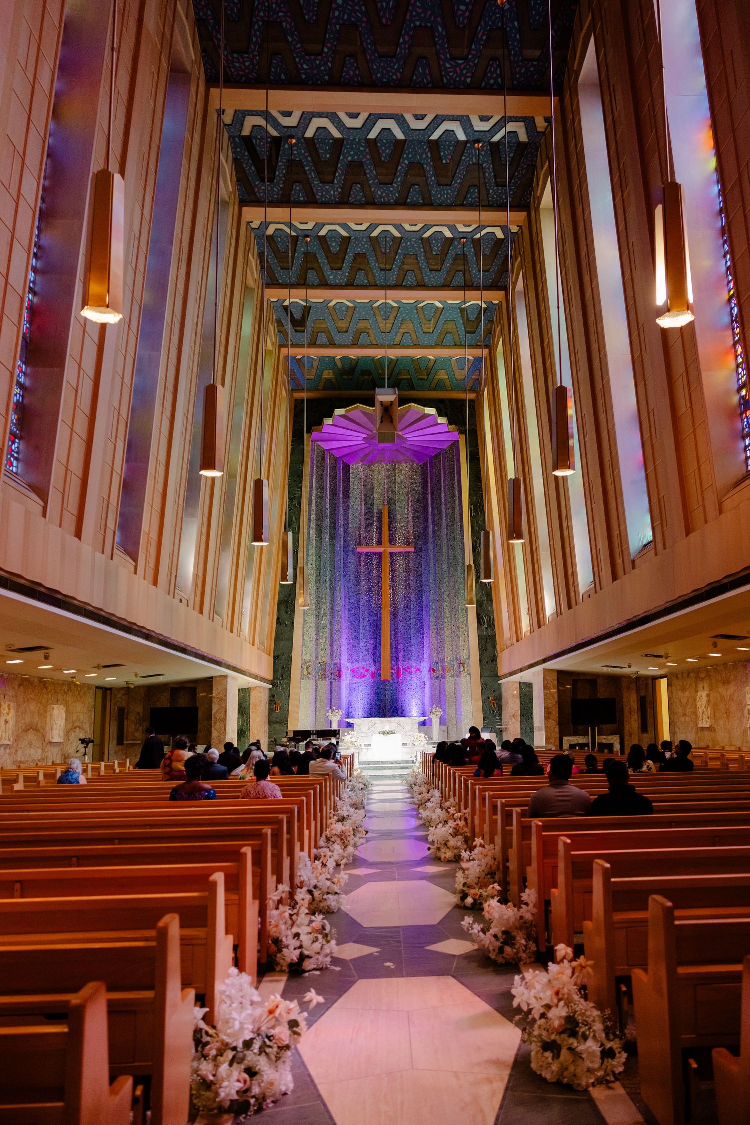 Church sanctuary decorated for wedding with purple lighting and white floral aisle arrangements.