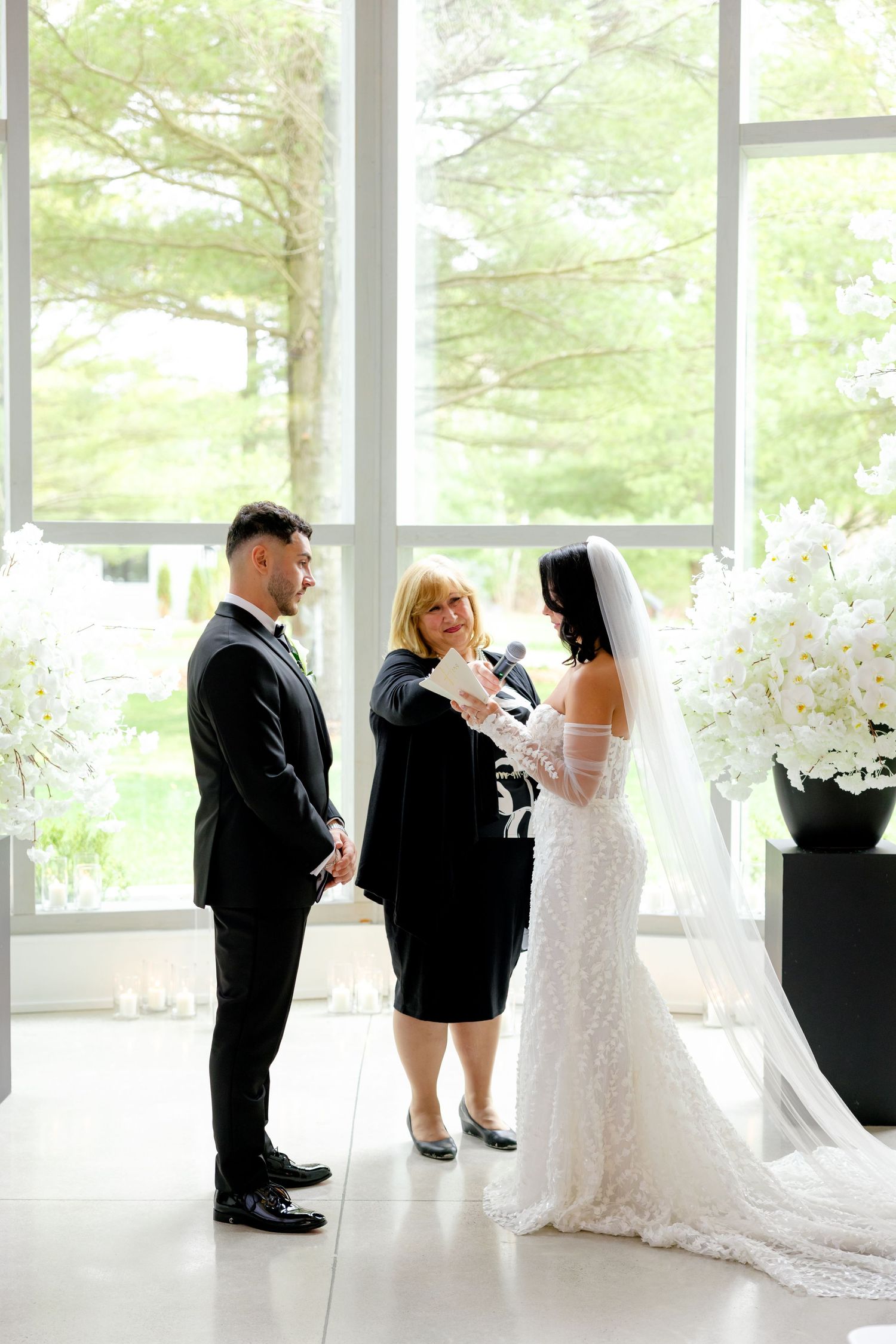 Wedding ceremony with officiant in black dress performing service in modern white venue.