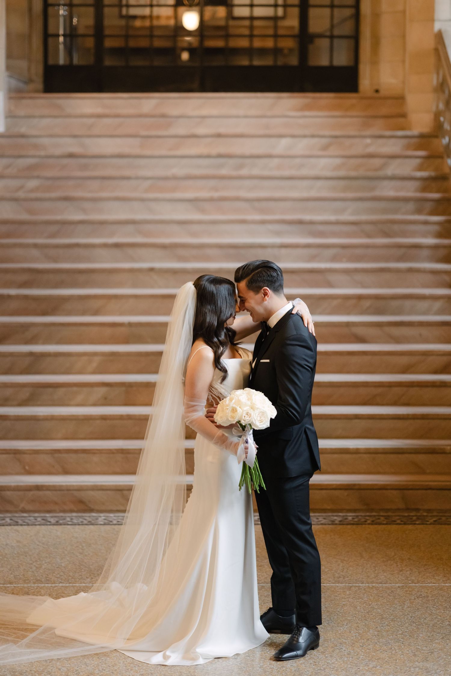 A tender wedding moment with white roses against the backdrop of an elegant marble staircase.