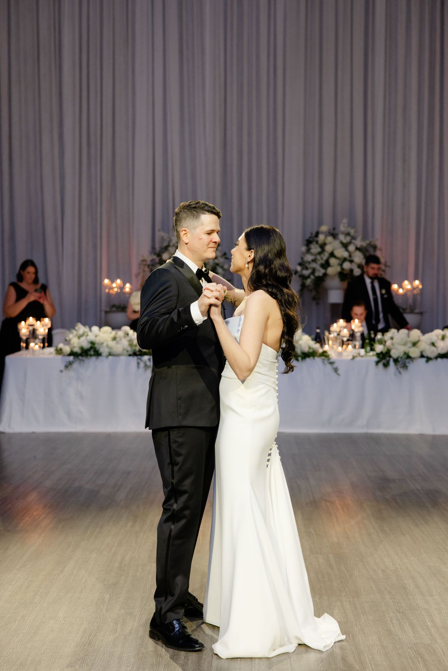 Elegant couple shares their first dance in reception hall decorated with floral arrangements.