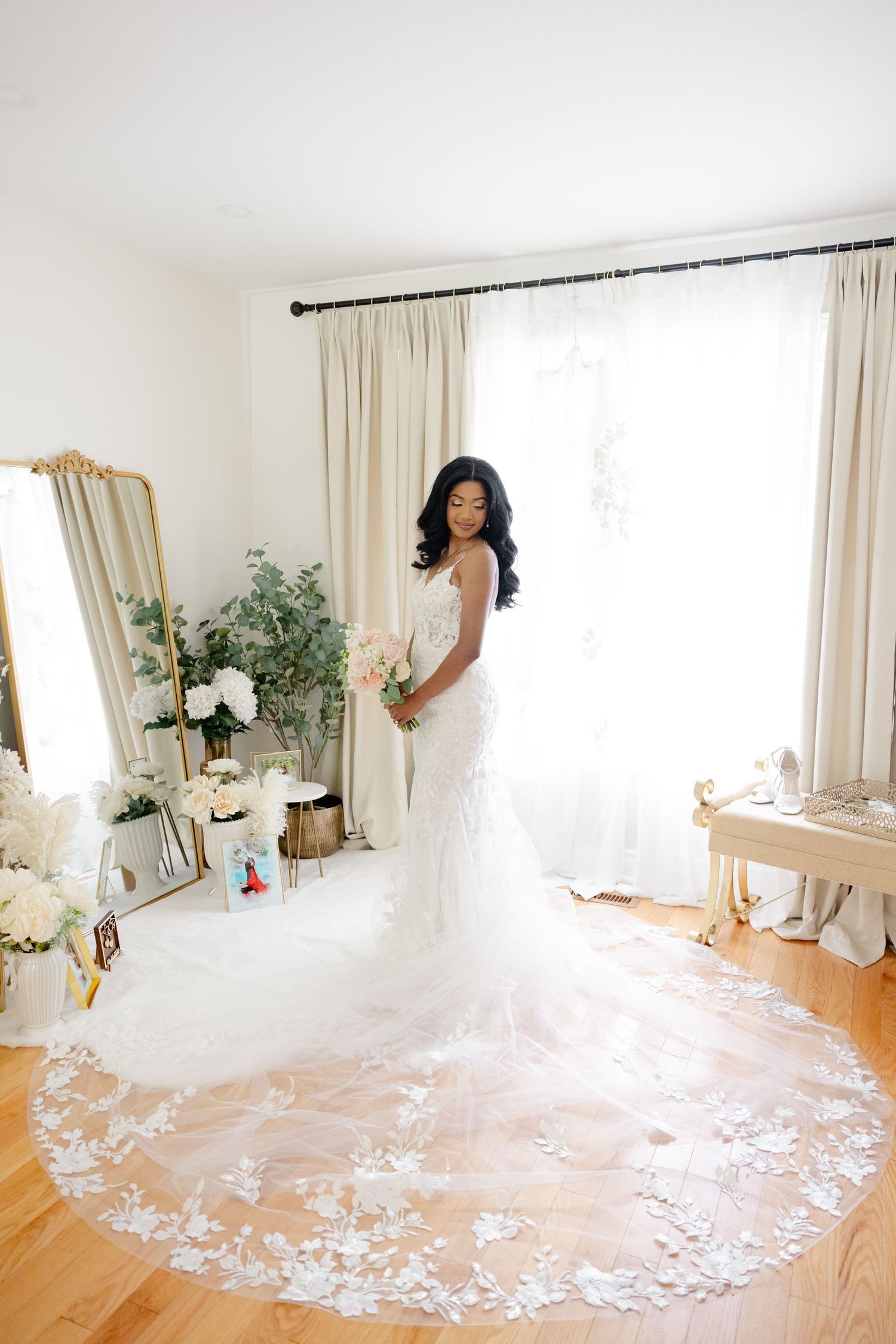 Elegant wedding gown with a dramatic lace train on hardwood floors in a bright white room.