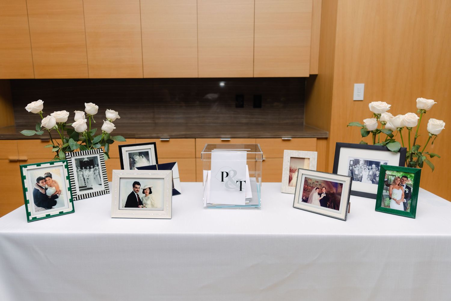 Wedding reception display table with framed photographs and white roses in elegant vases.