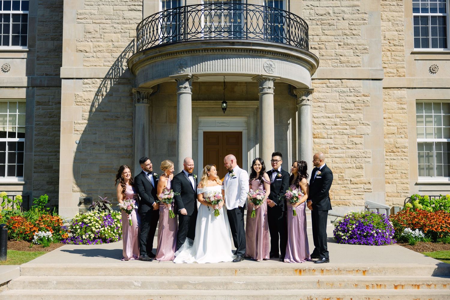 Bridal party gathered on stone steps of elegant classical building.