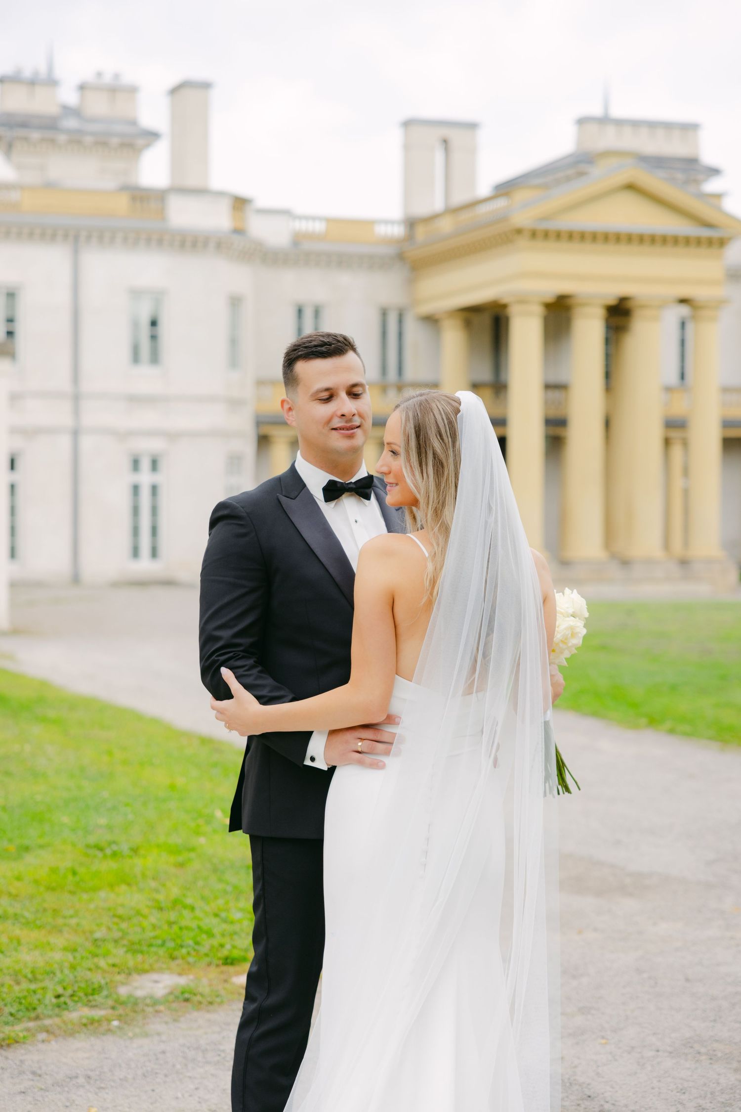 Wedding couple poses in front of grand neoclassical mansion with columns.