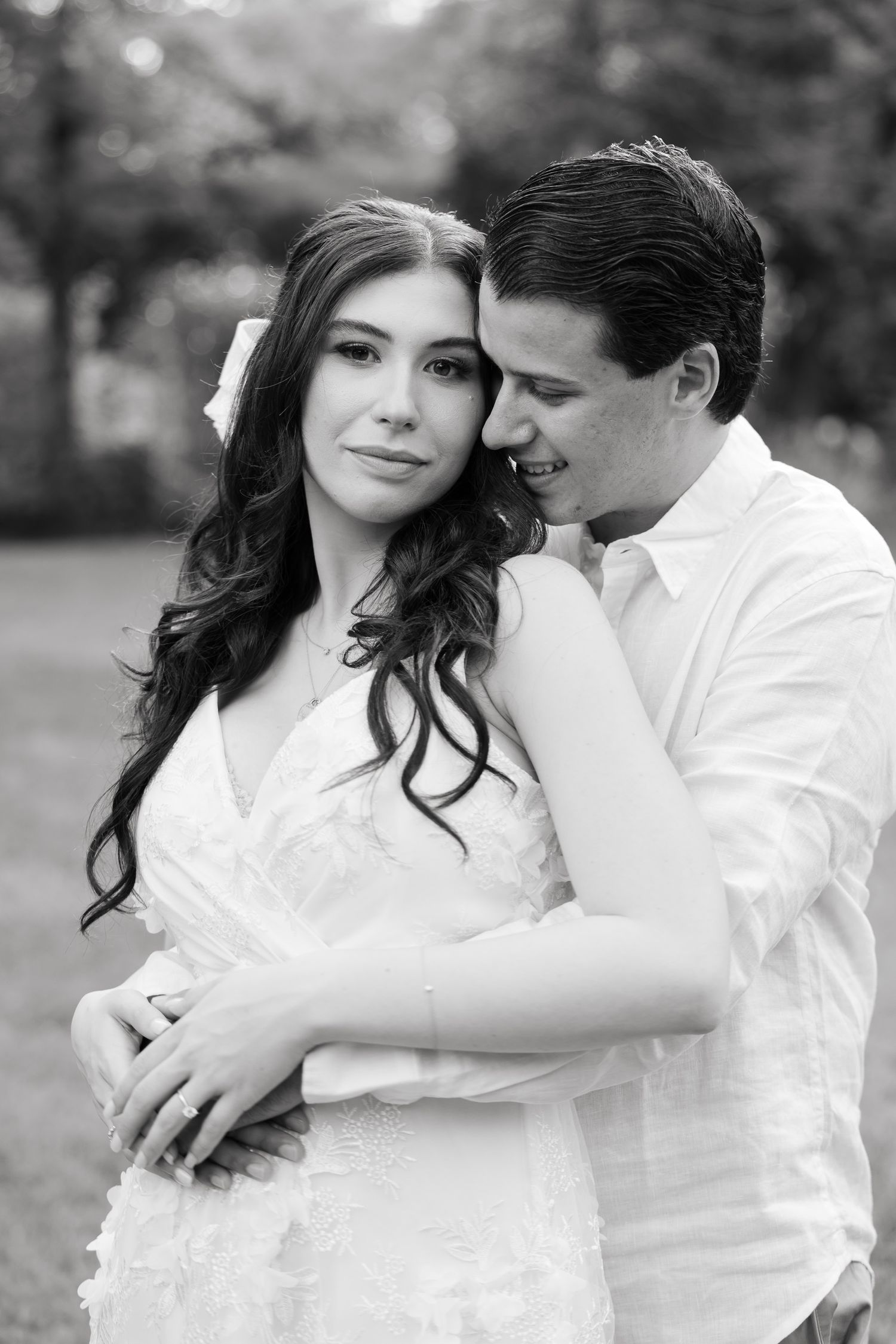 Elegant black and white portrait of couple in white attire against natural outdoor backdrop.
