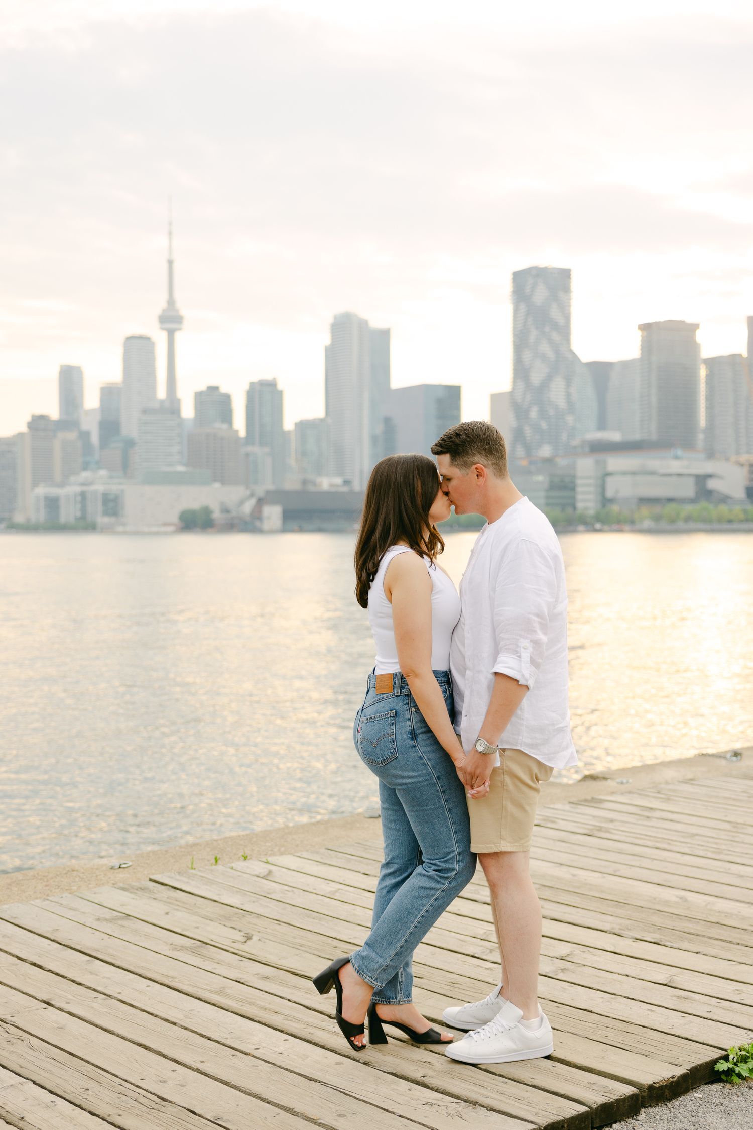 Romantic pose on wooden boardwalk with Toronto waterfront view at sunset.