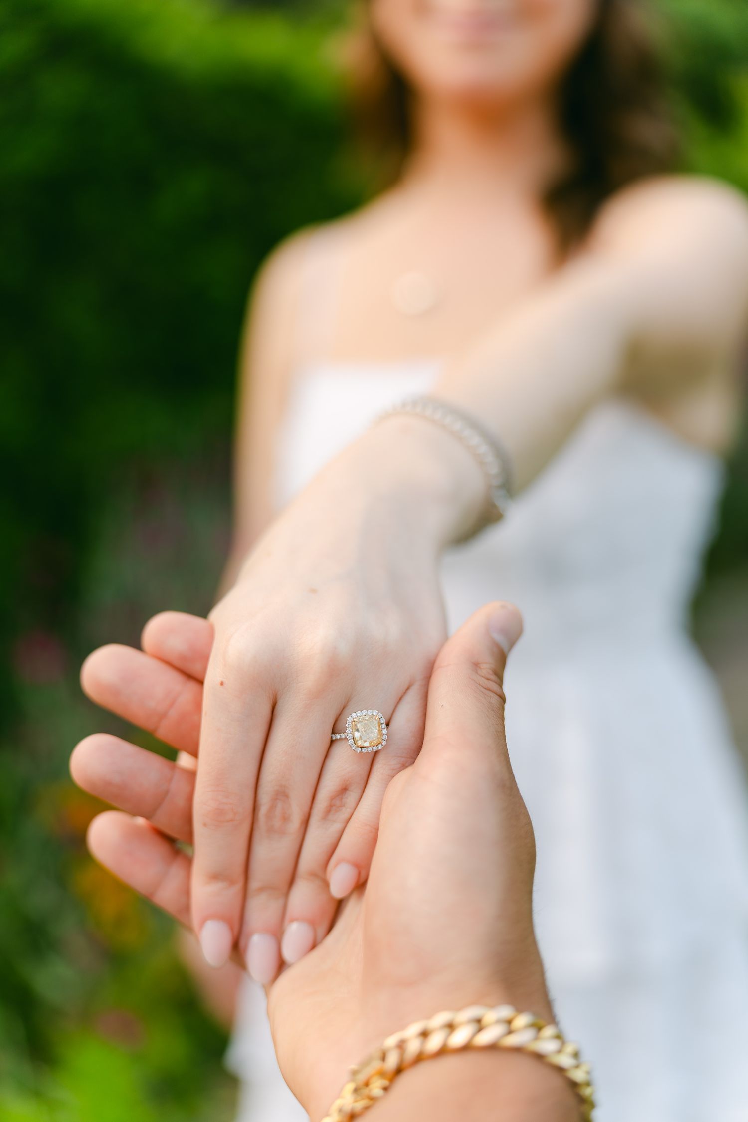 Detail shot of engagement ring and gold bracelet with garden backdrop.