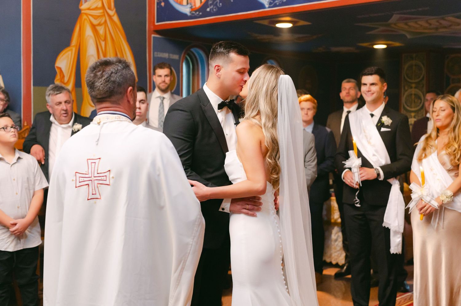 Intimate moment during Orthodox wedding ceremony with priest and gathering of guests.