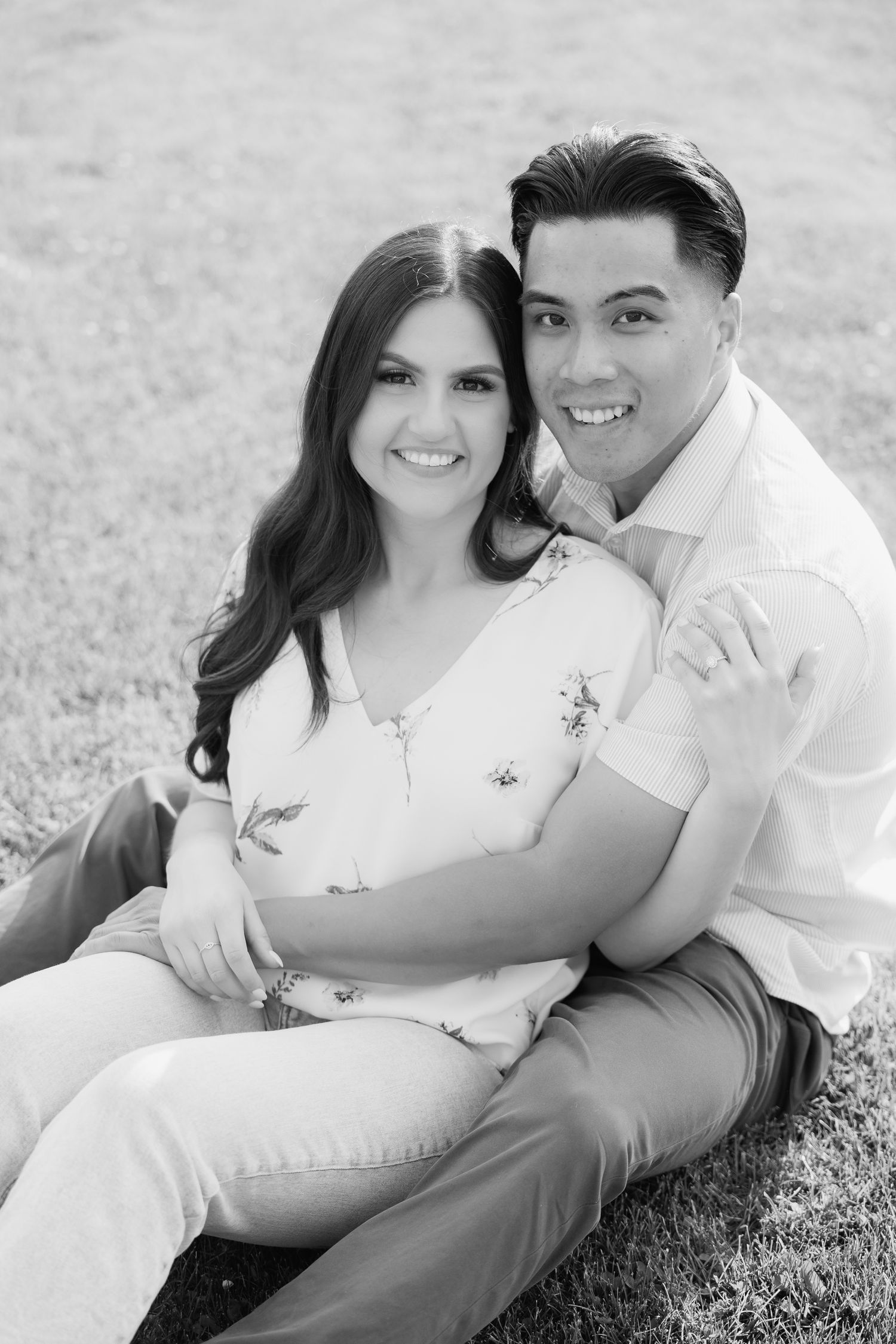 Couple in white outfits sharing an intimate black and white portrait while sitting on grass.