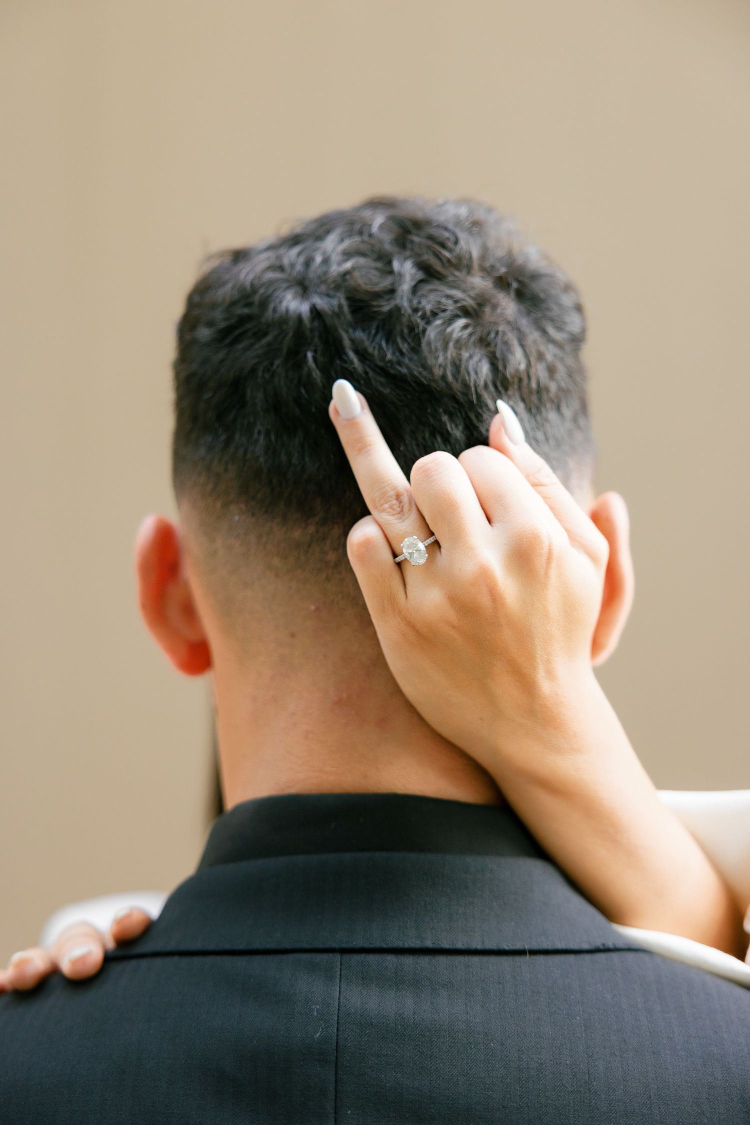 Close-up of a hand with an engagement ring running through dark hair.