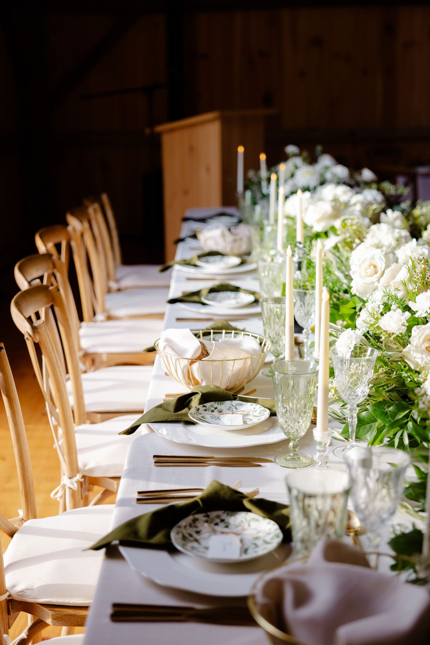 Elegant table setting with white linens, wooden chairs, and white floral centerpieces.