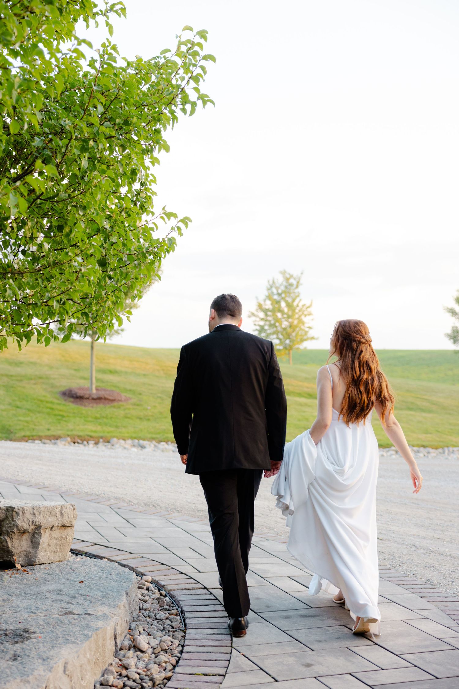 Couple walking along curved stone path surrounded by green landscaping.