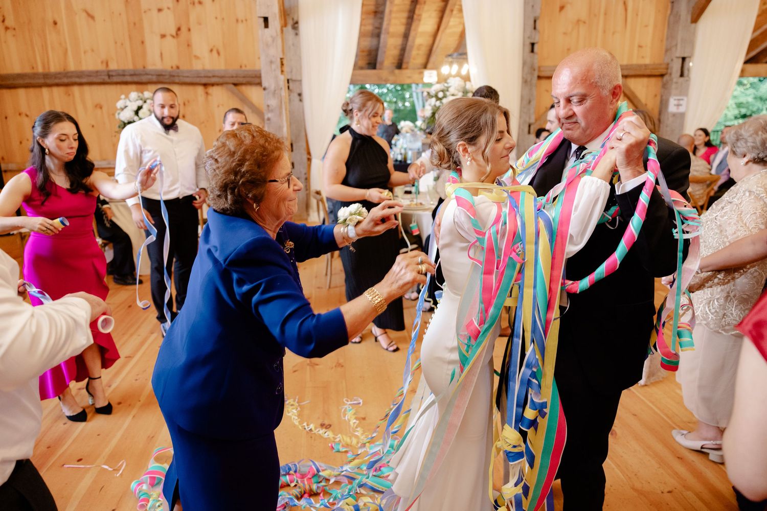 Wedding celebration with colorful streamers and guests dancing in a wooden barn.